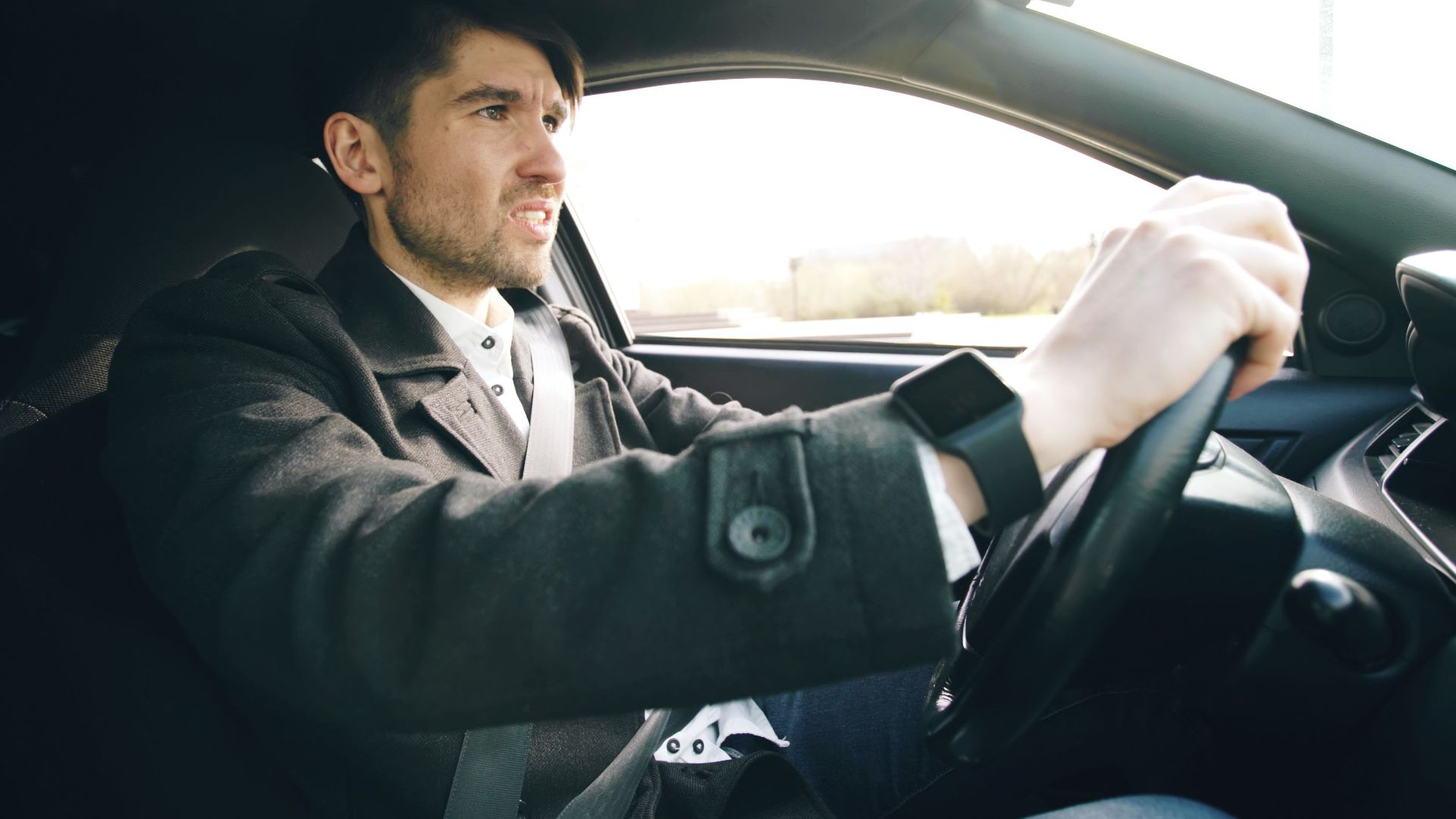 A man driving a car, wearing a wristwatch, focused on the road.