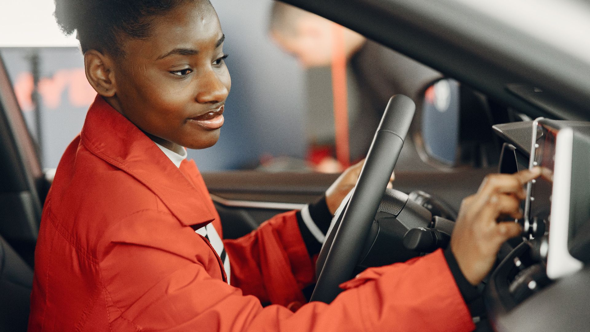 Young woman in red coat using touch screen in car interior.