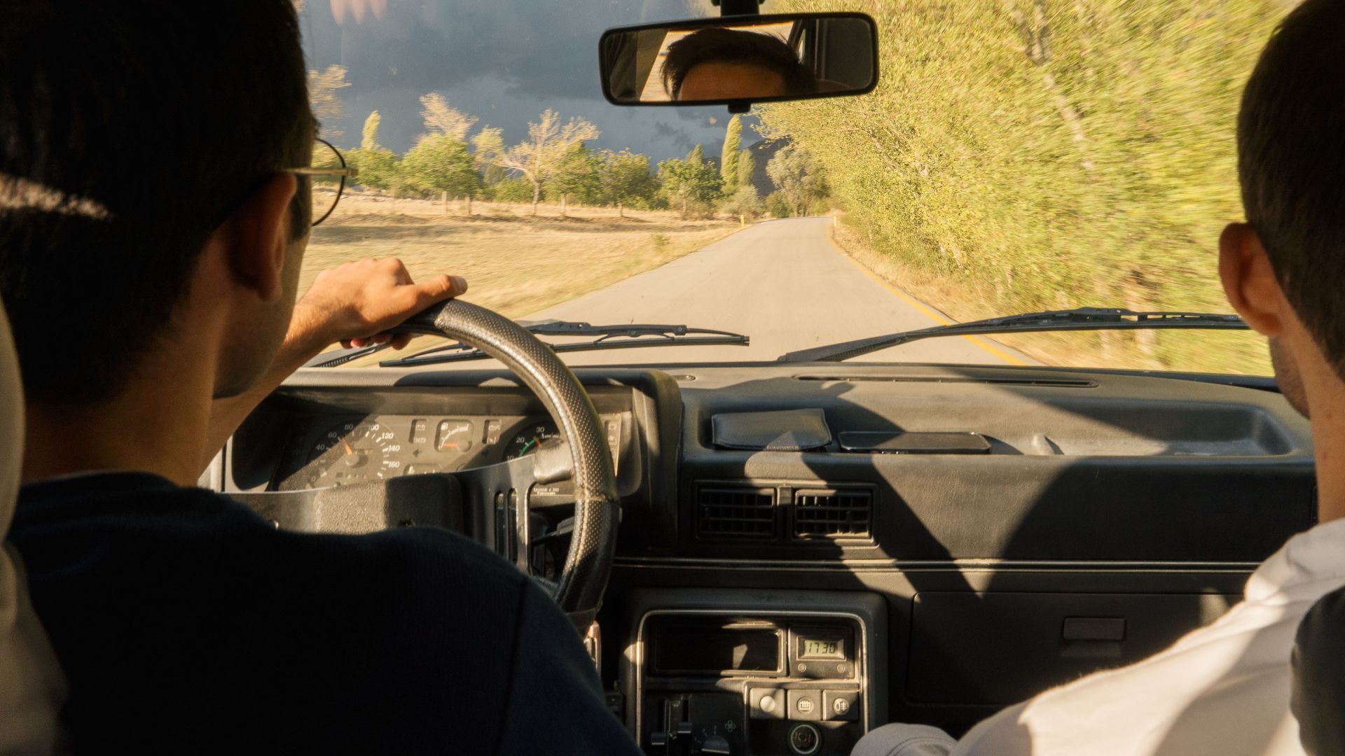 Two adults driving through scenic countryside near Merzifon, Türkiye, in a vintage car.