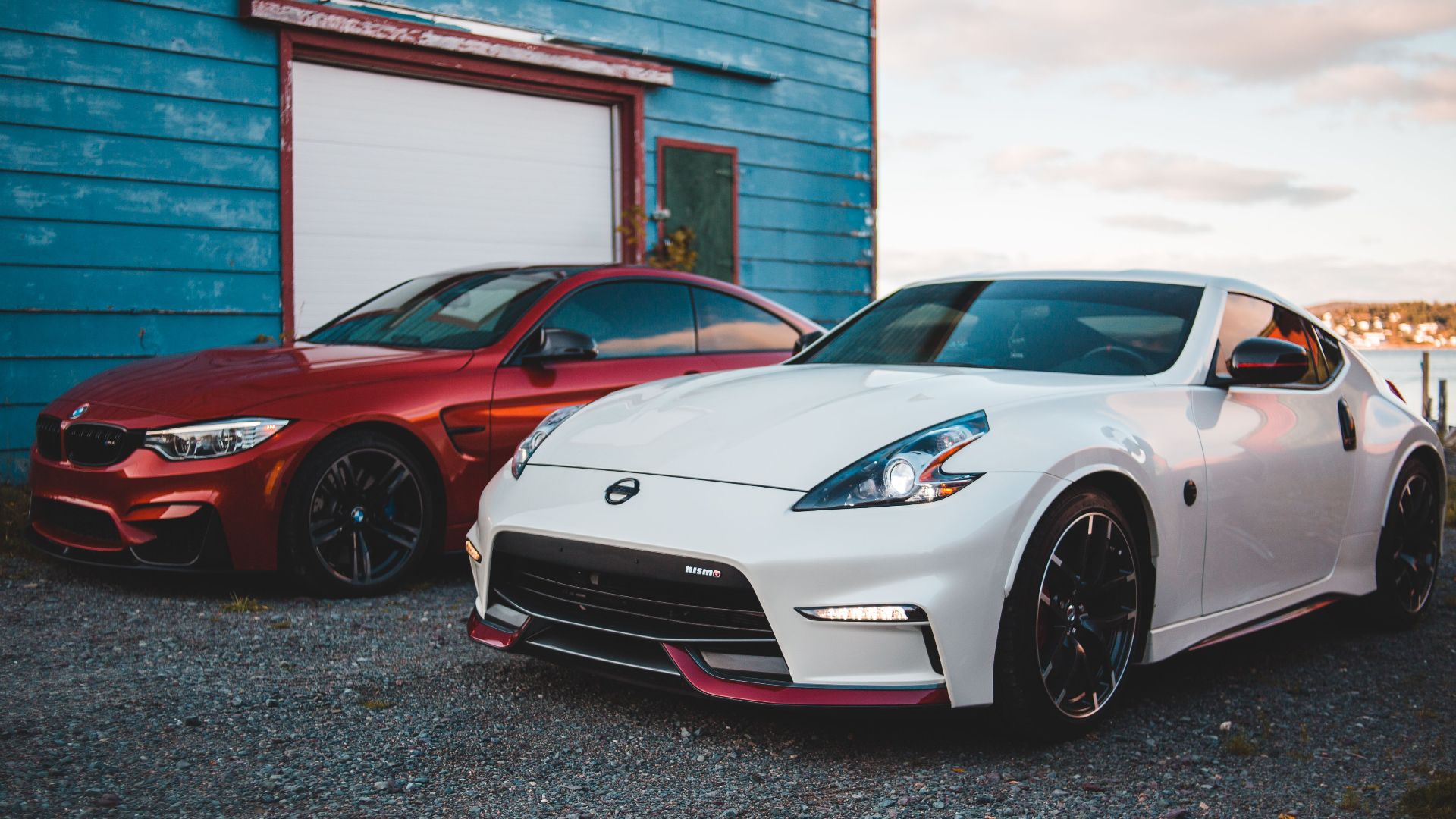 Stylish shiny tuned red and white sports cars parked near rustic barn at lakeside in suburb area