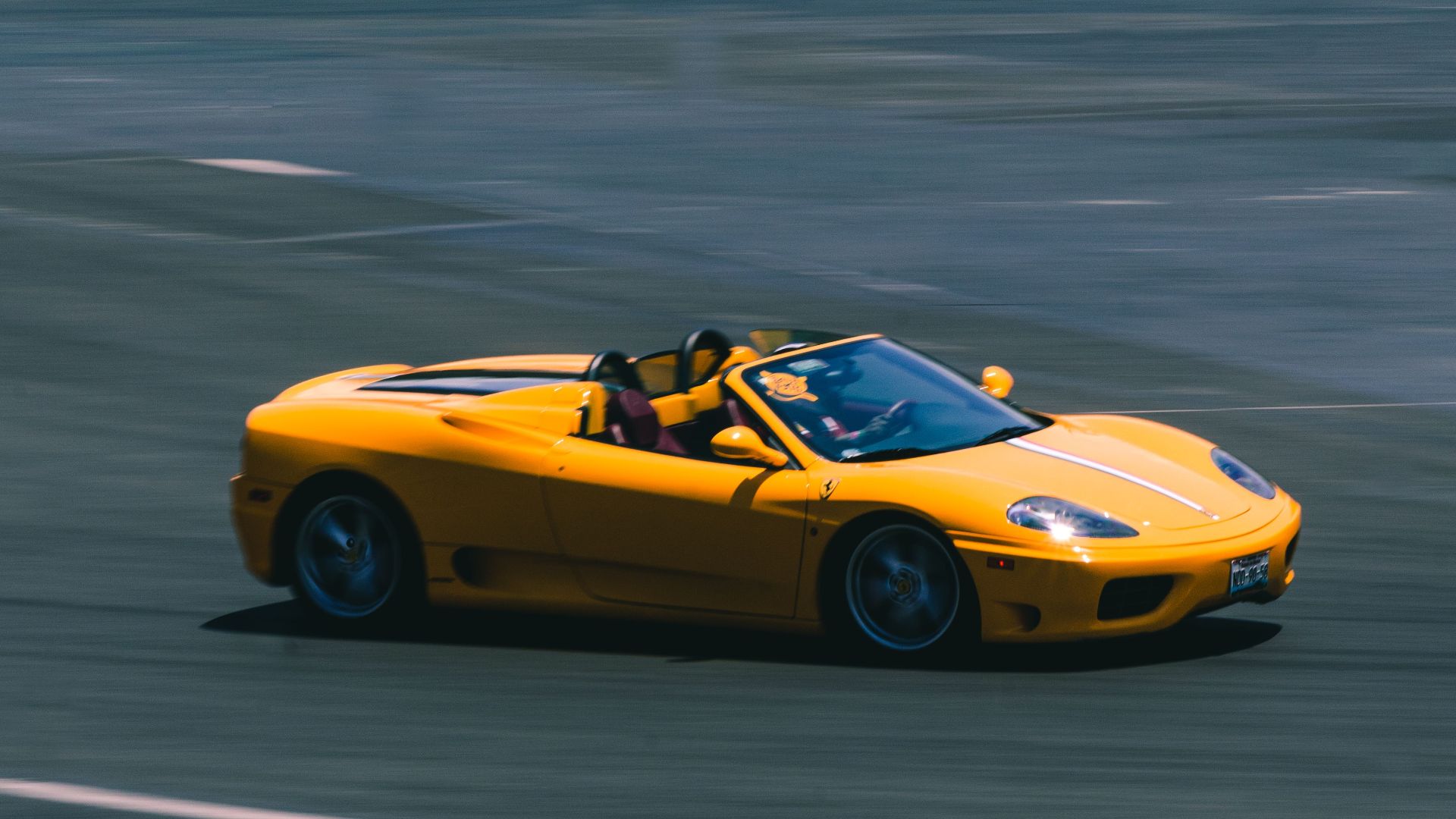 A vibrant yellow convertible sports car speeding on a racetrack, showcasing blurred motion and high speed.
