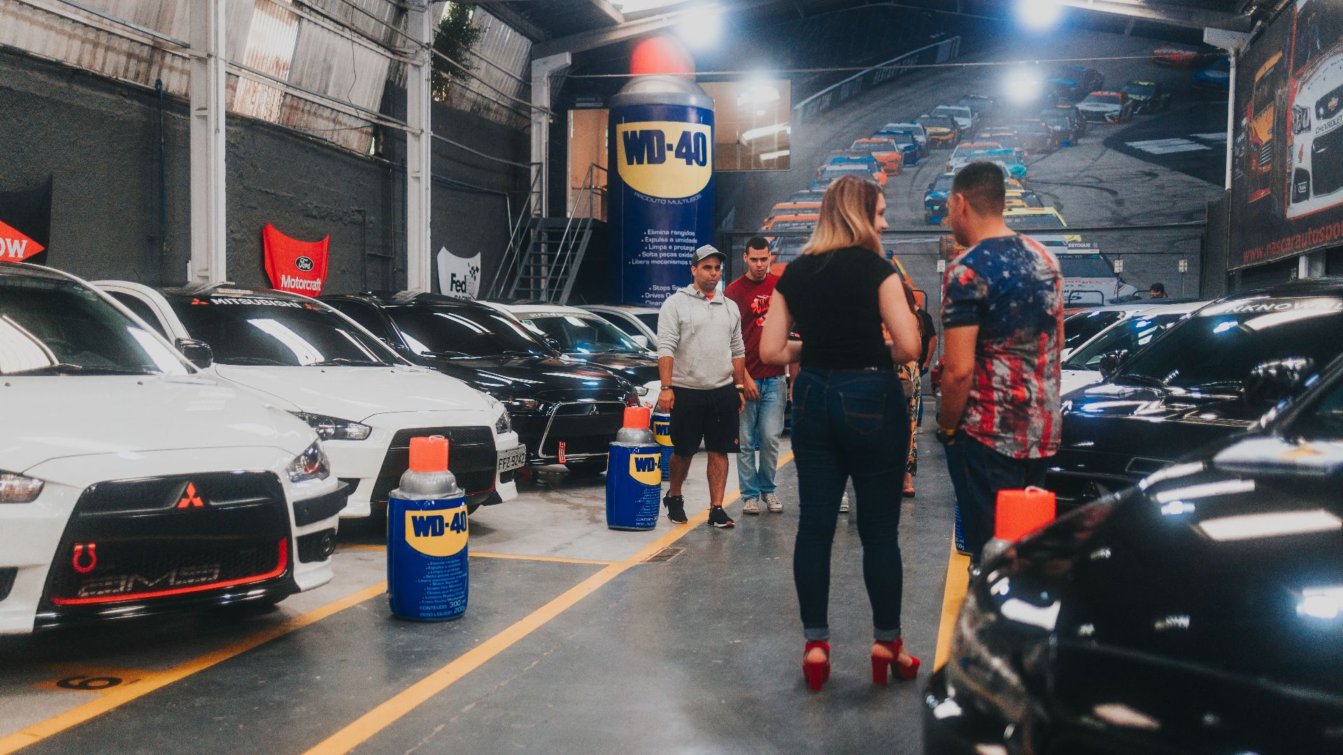 People inspecting lined-up Mitsubishi Lancer Evolutions in an indoor car show garage.