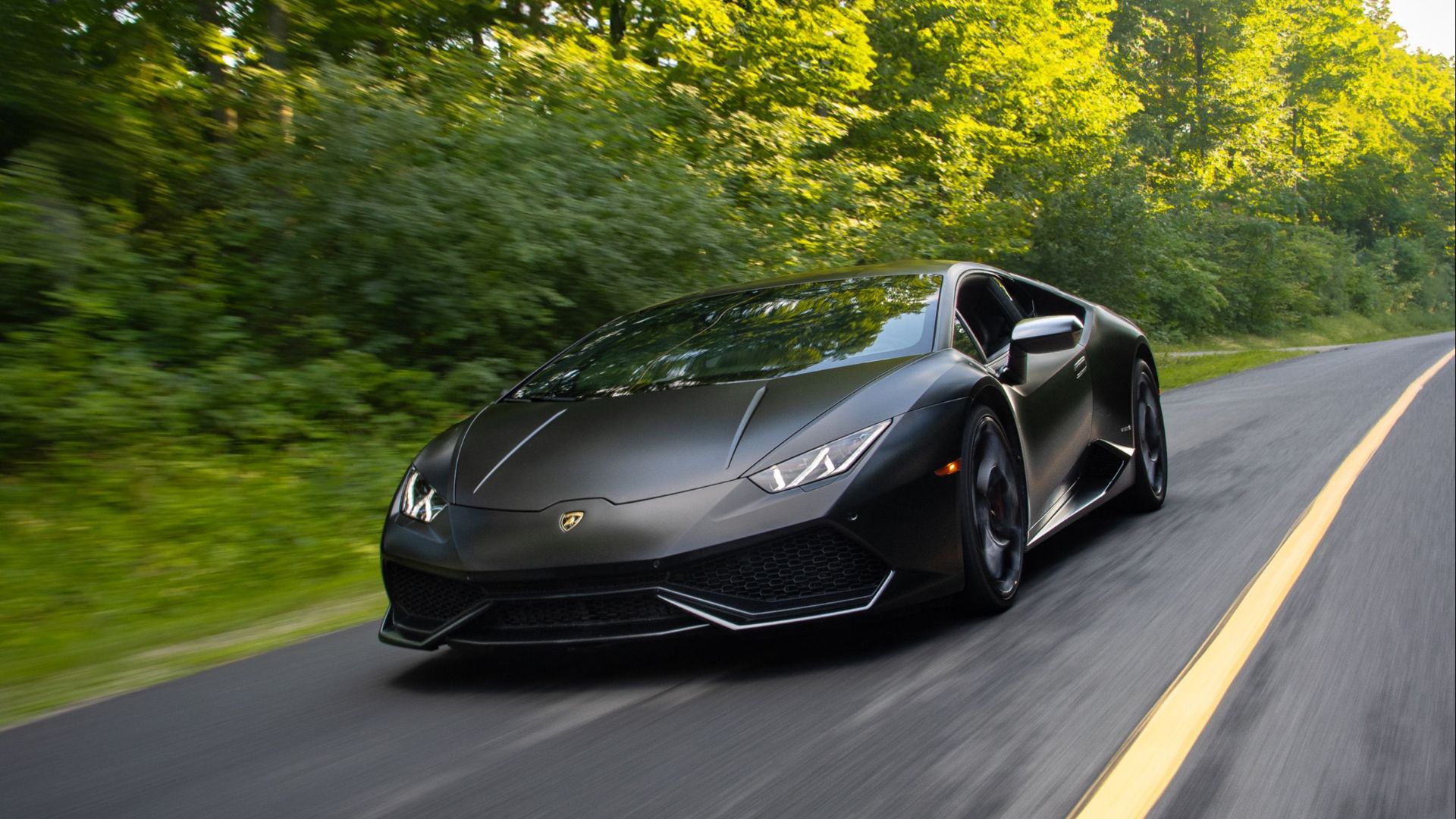 A high-performance black sports car speeds down a scenic, tree-lined country road.