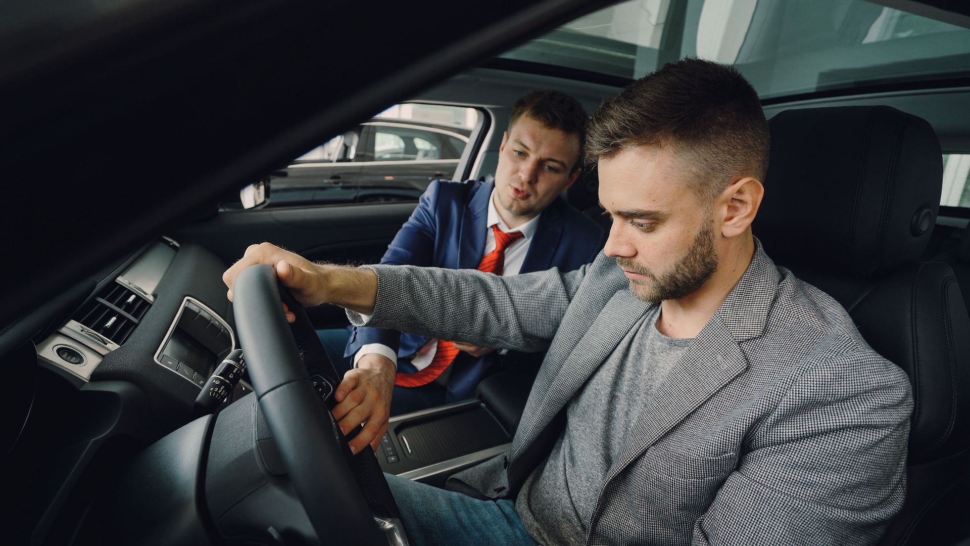 Salesman demonstrating car features to potential buyer inside vehicle showroom.