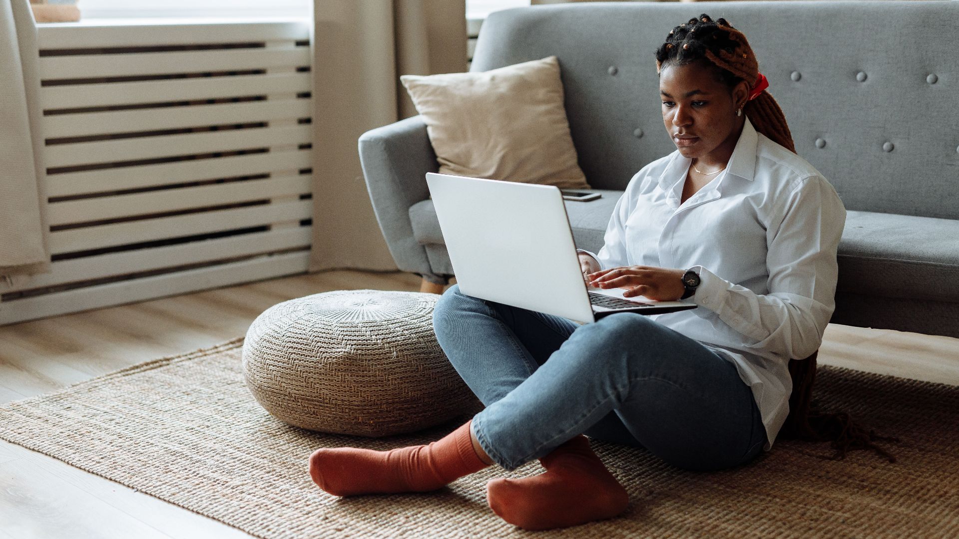 African American woman sitting on floor working from home on laptop in a cozy living room.