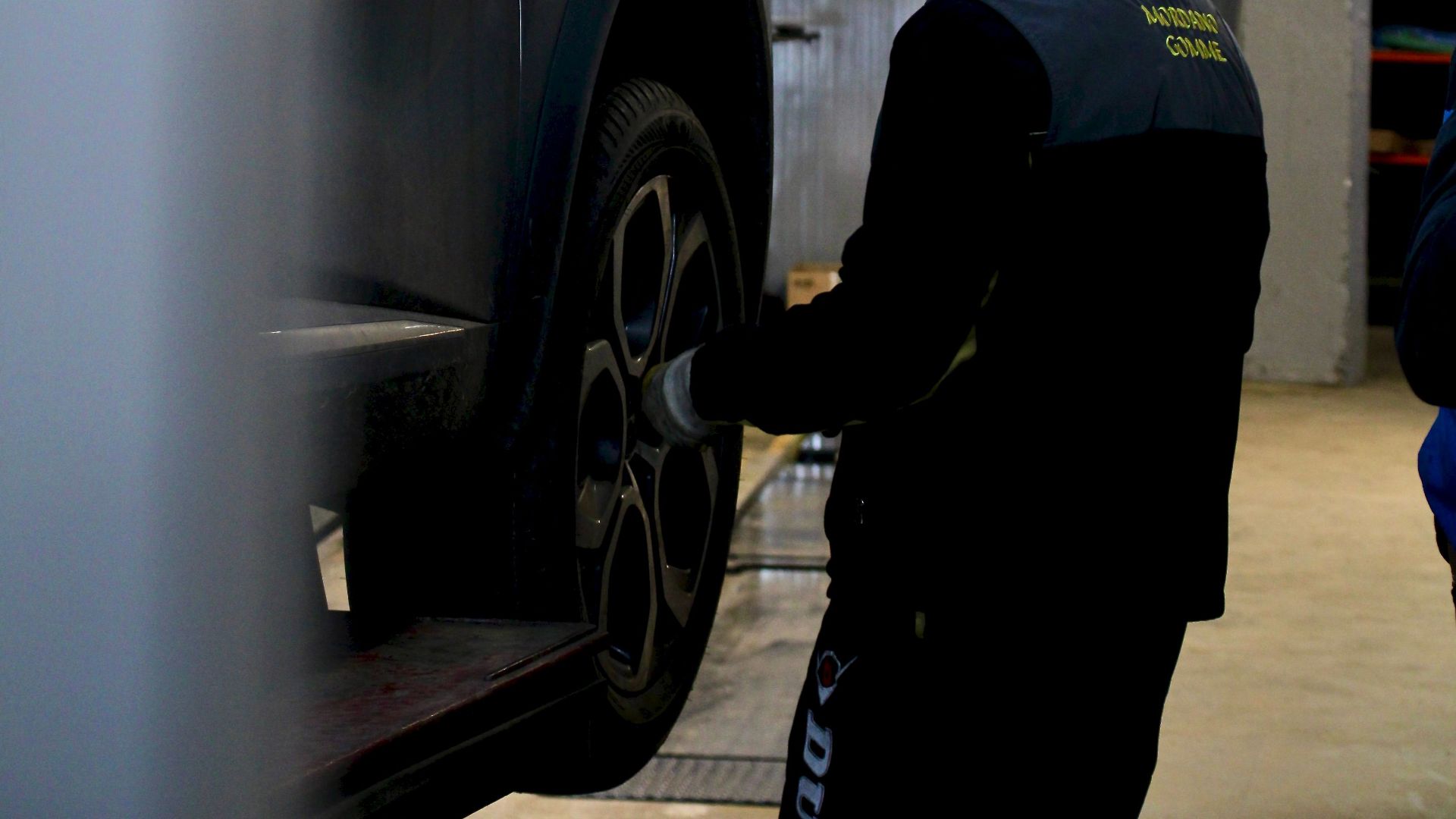 Mechanic adjusting car tire on lift in an indoor workshop setting.
