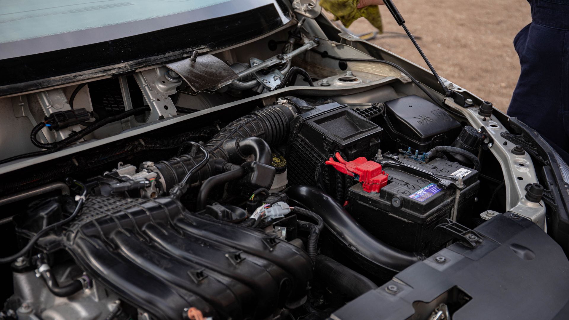 Mechanic inspecting car engine bay and battery during routine maintenance.