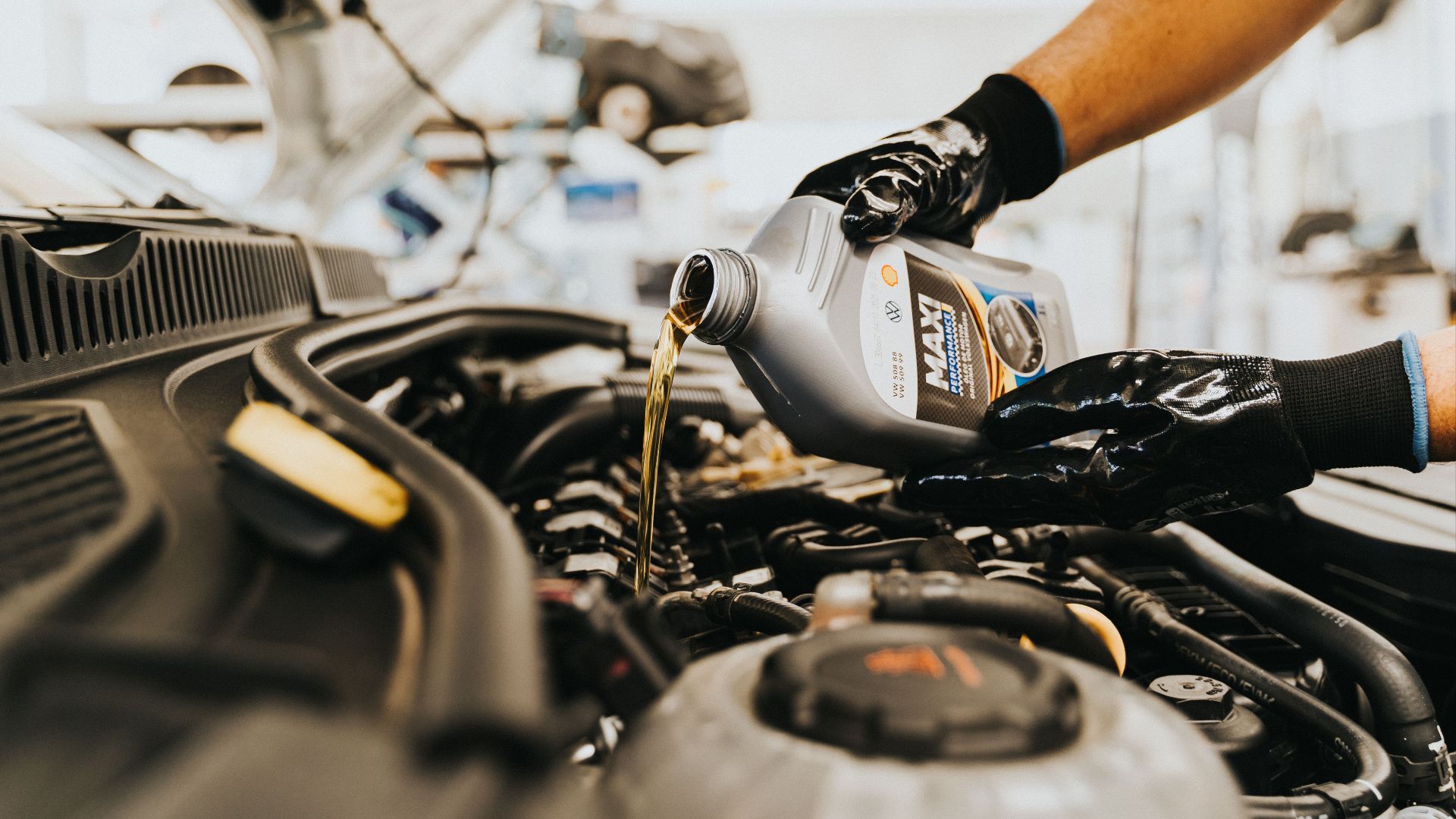 Close-up of a mechanic pouring engine oil into a car engine in an auto repair shop.