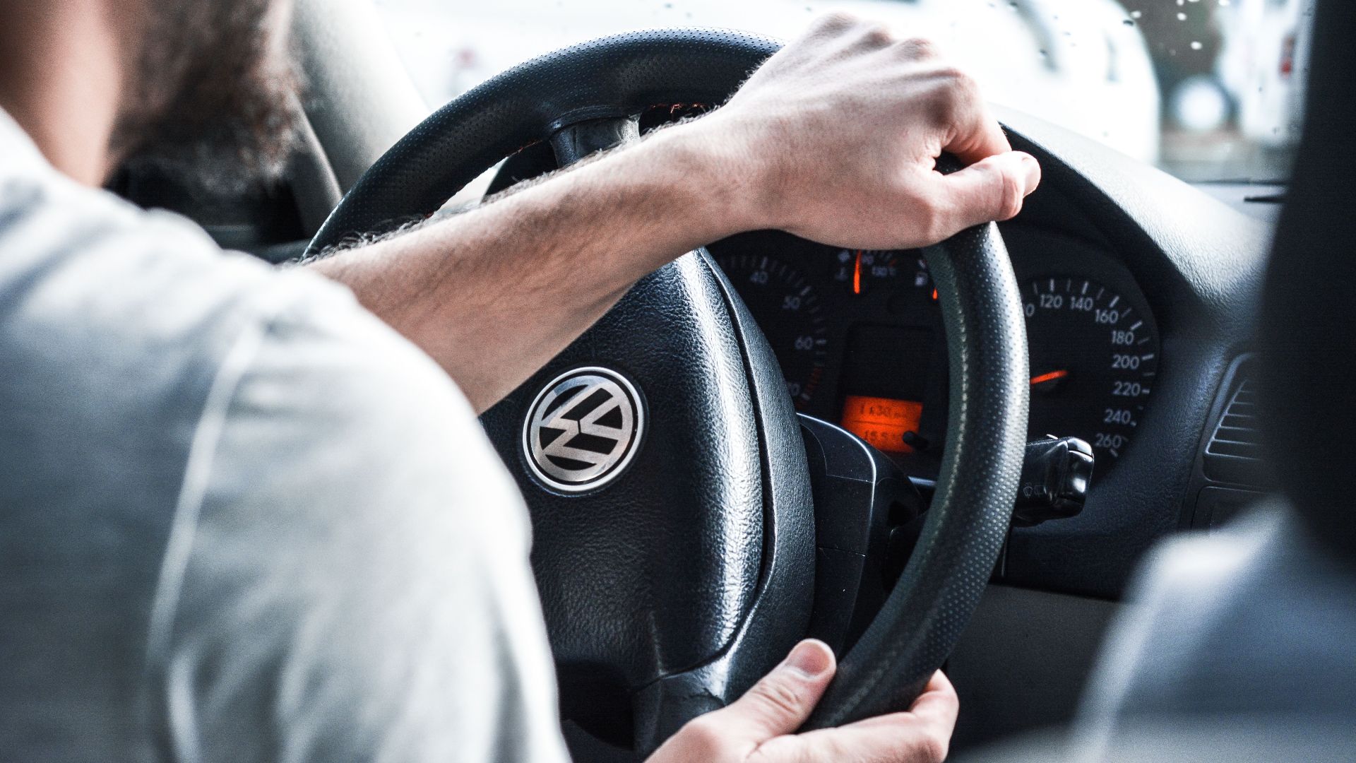 Man gripping Volkswagen steering wheel, focused on driving and vehicle interior details.