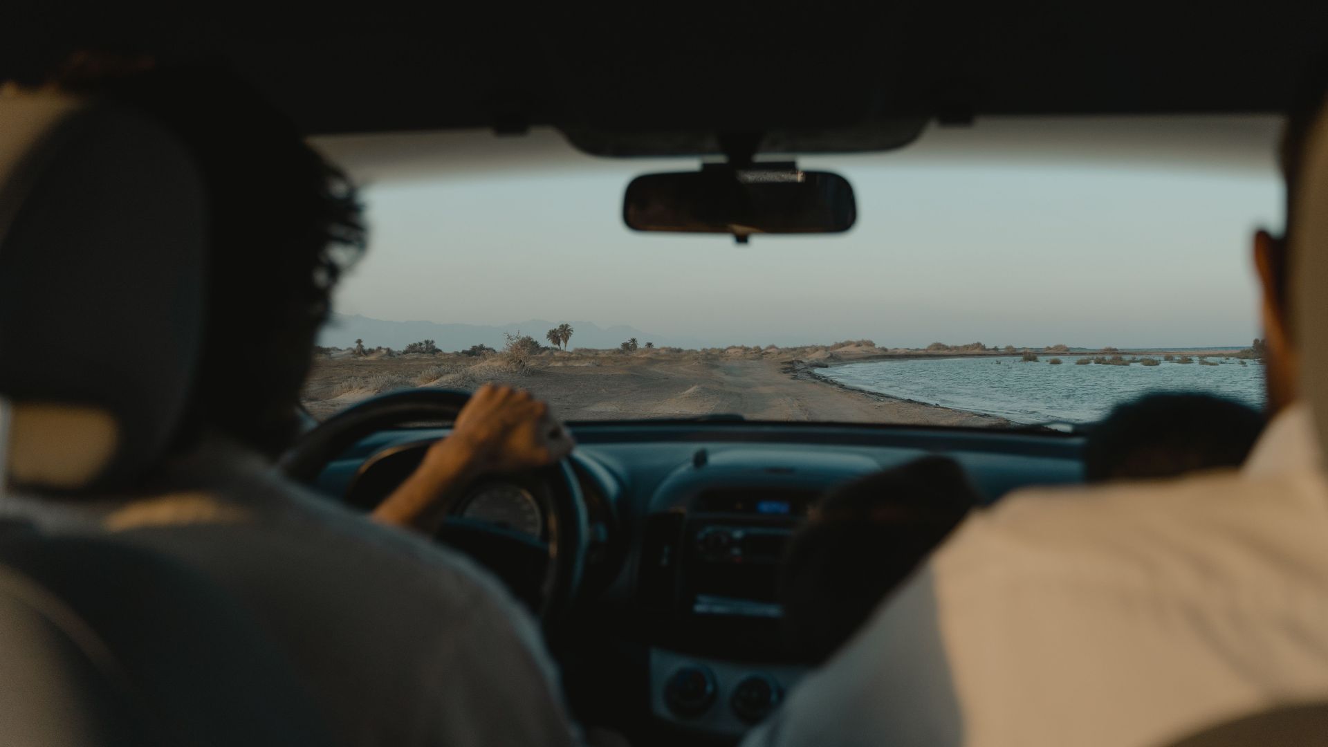 Interior car view of a scenic drive along a coastal road at sunset.