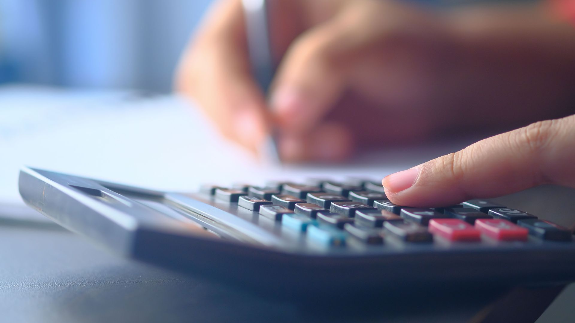 A close-up image of hands working on a calculator and writing, representing budgeting and financial planning.