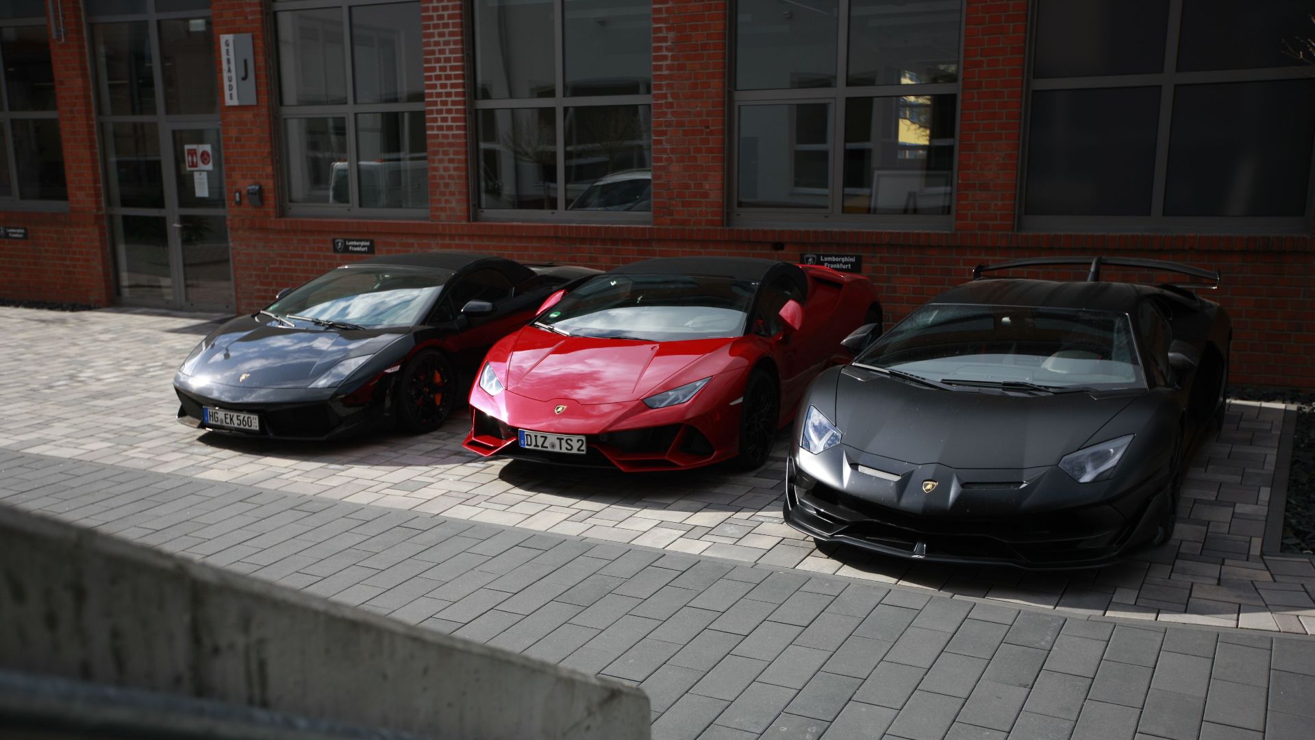 Three sleek Lamborghini supercars parked outside an urban building.