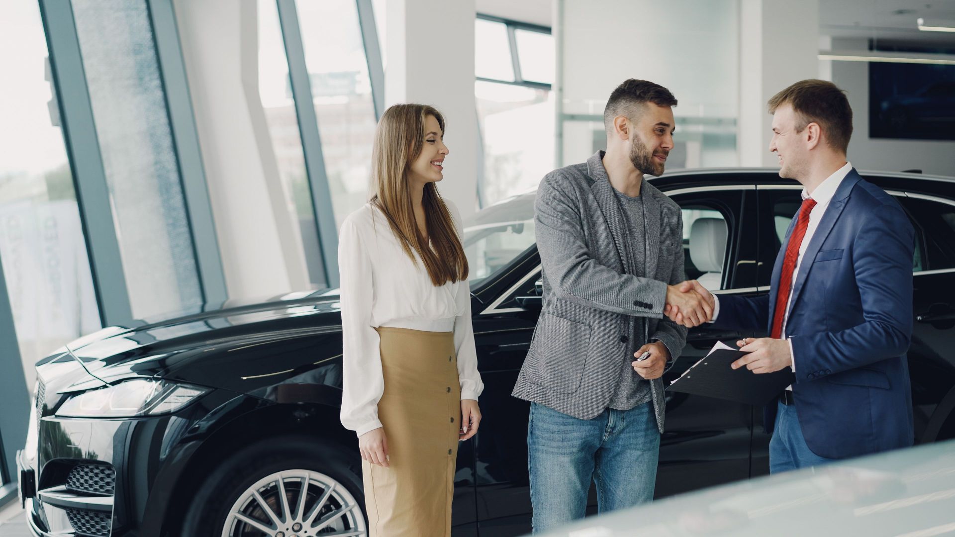 Customers shaking hands with dealer in showroom, sealing car purchase deal.