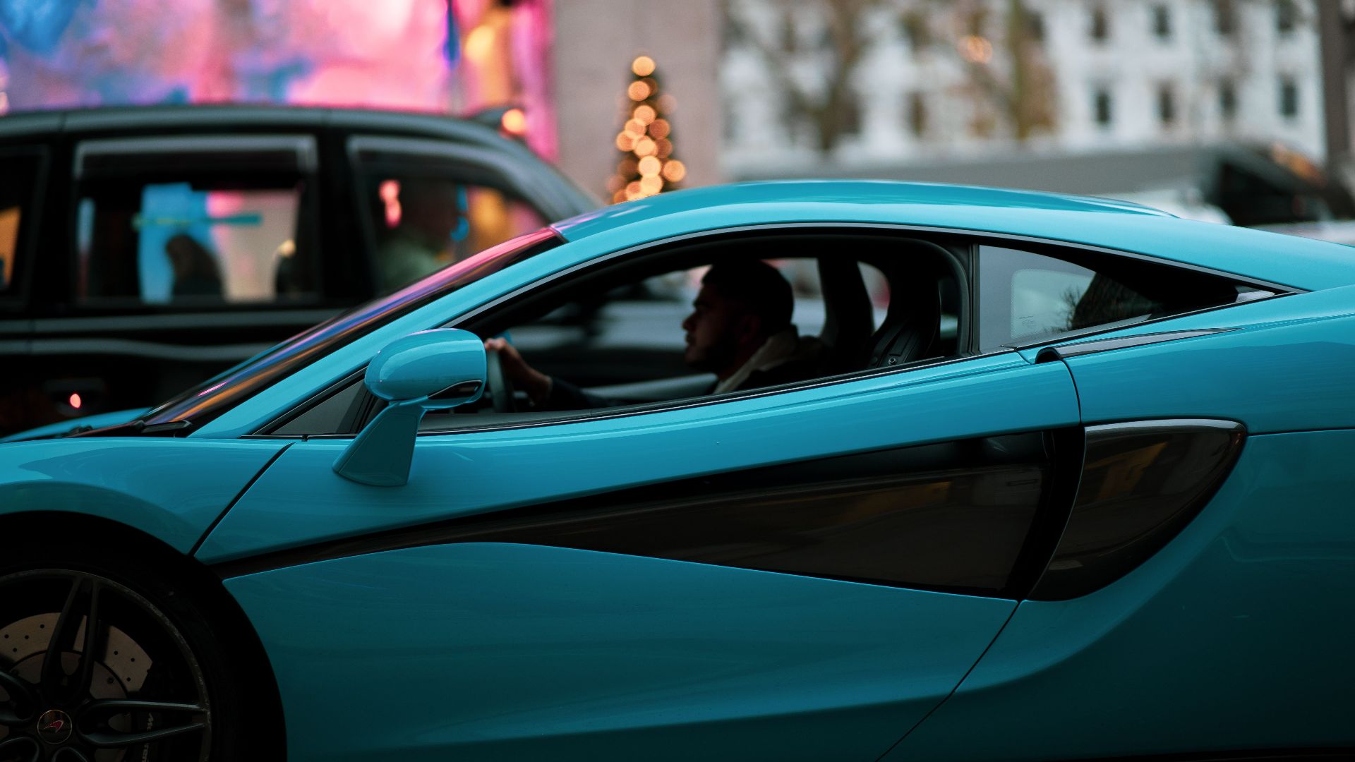 A blue supercar navigates the busy streets of London, showcasing luxury automotive design.