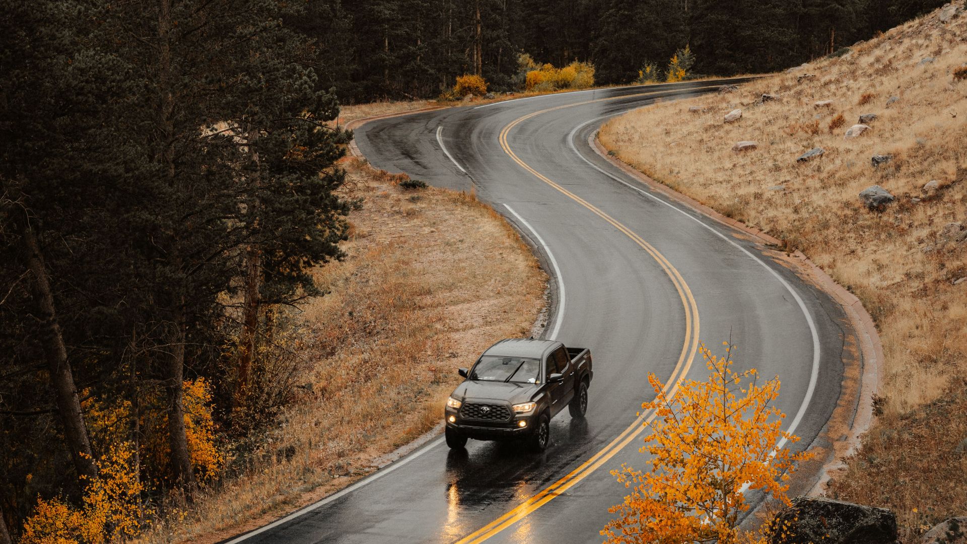 Car driving on a winding mountain road in autumn, surrounded by fog and vibrant foliage.