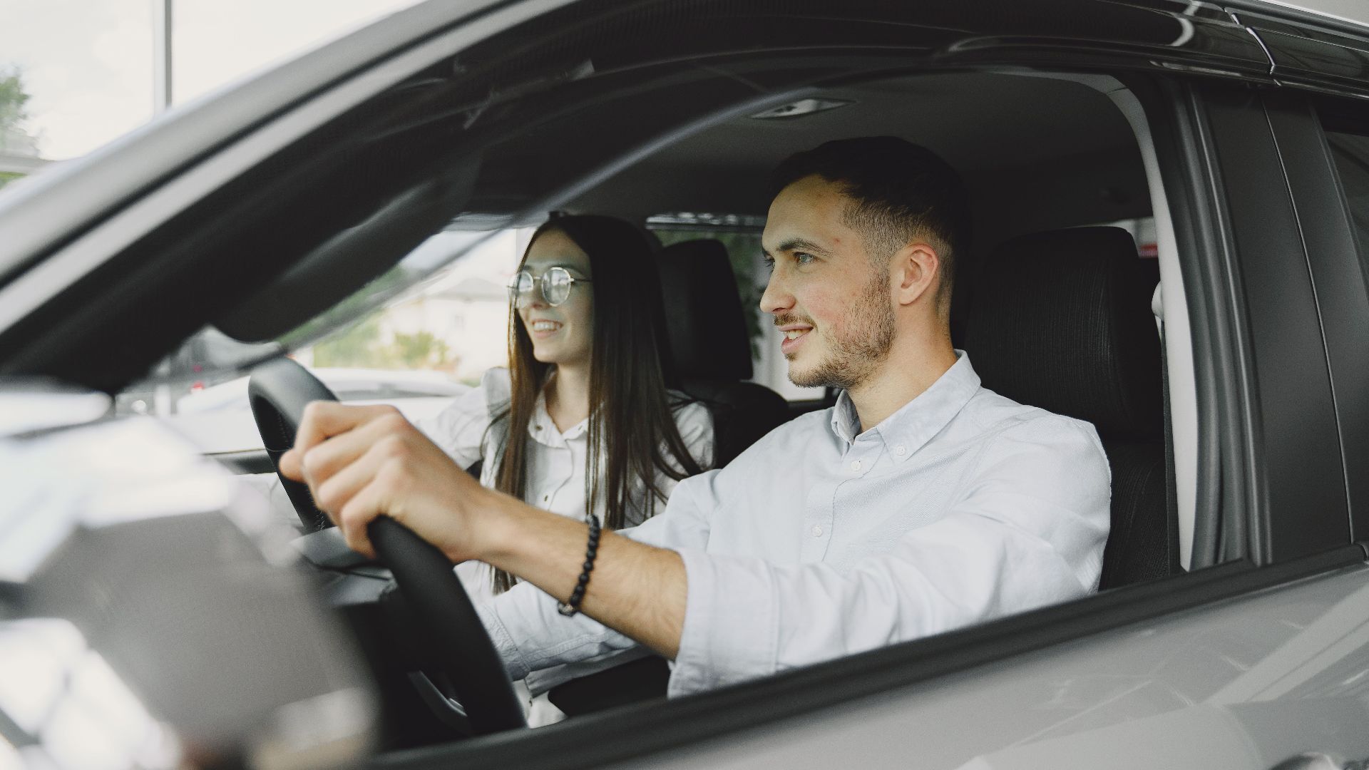 A young couple smiling while driving together in a modern car interior.