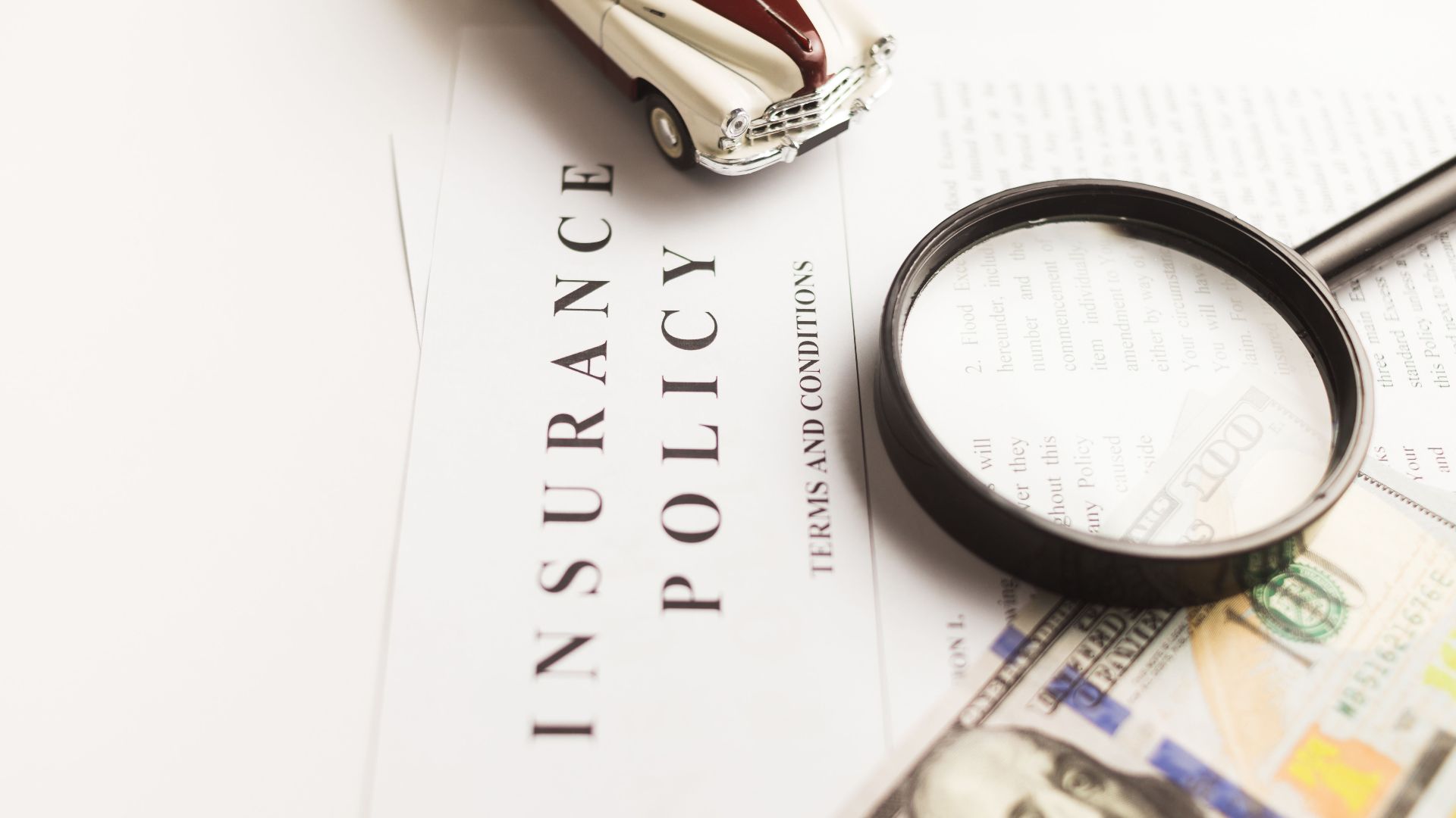 Close-up image of an insurance policy with a magnifying glass, money, and toy car.