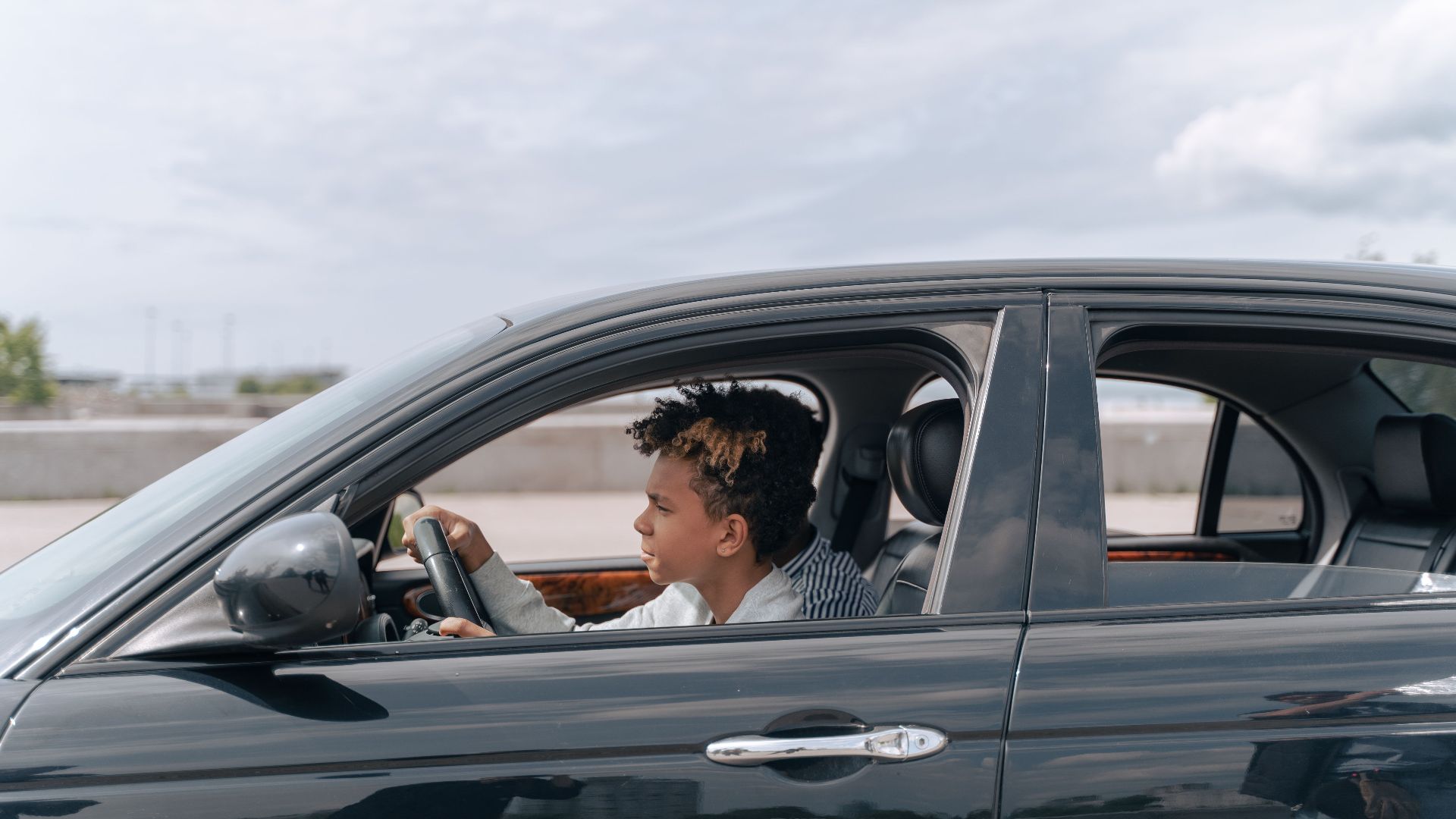 Side view of a young male teenager focused on driving a car in bright daylight.