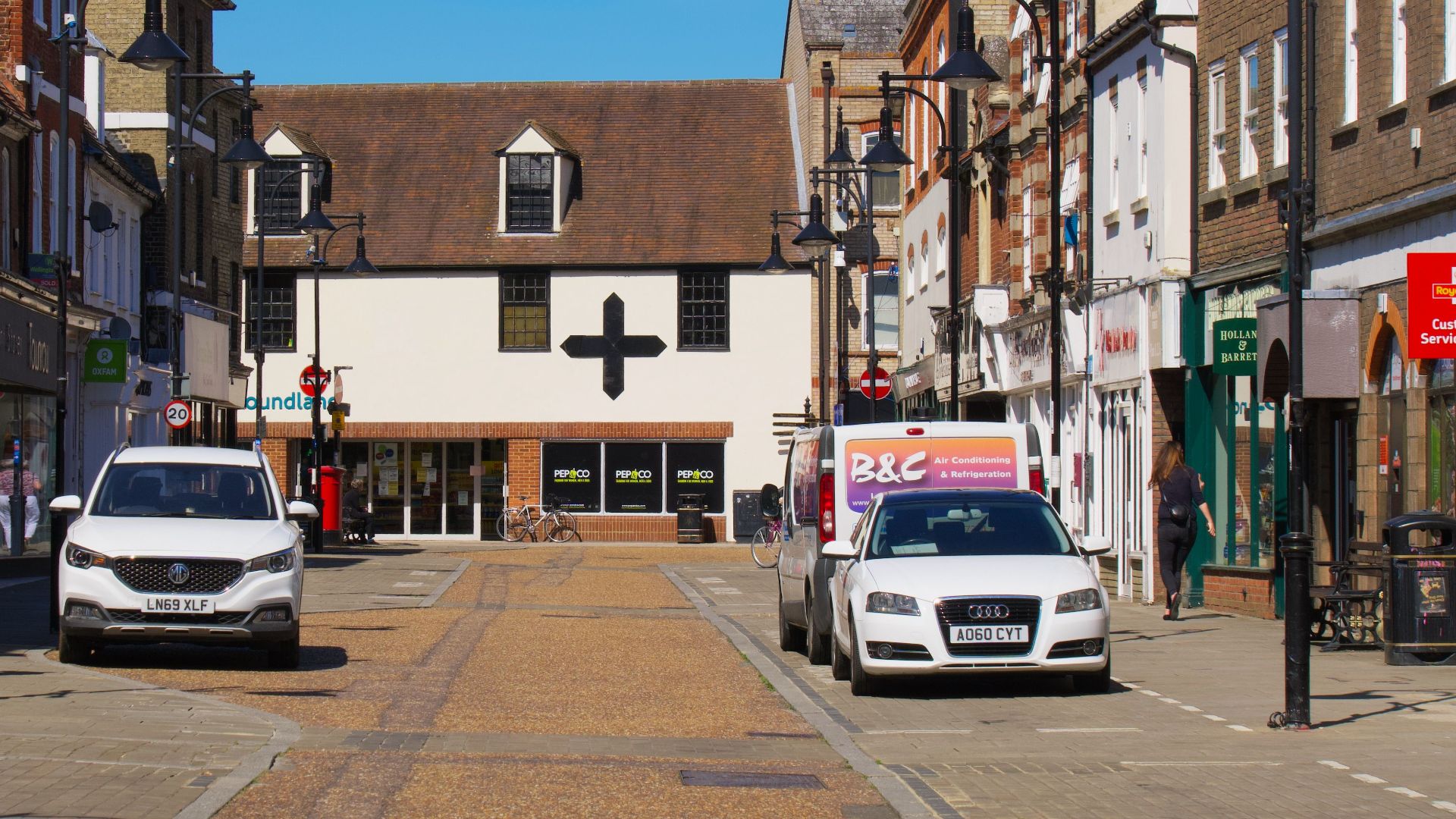 Sunny day on a lively street in Cambridge, England showcasing shops and parked cars.