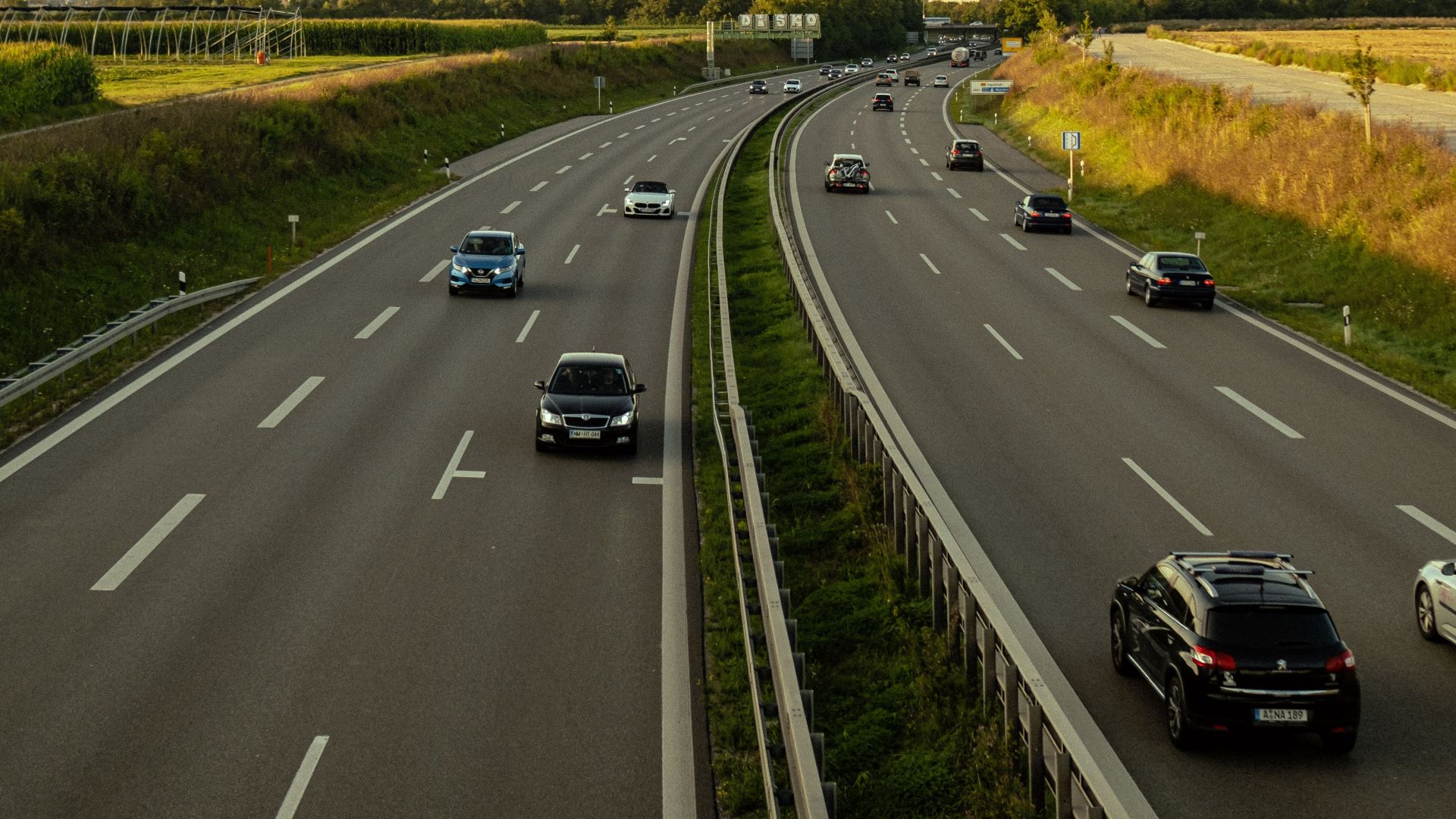 Cars driving on a busy highway under a clear, blue sky with greenery around.