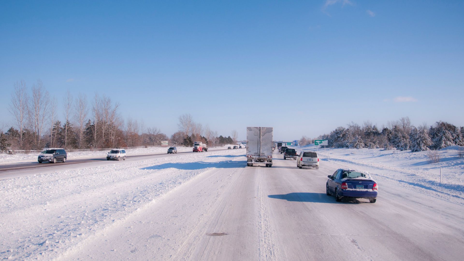 Cars and trucks driving on a snowy highway during winter daytime.