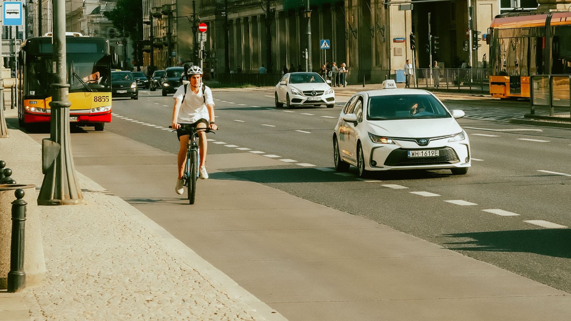 A bustling Warsaw street with cyclists, cars, and the MDM Hotel under a partially cloudy sky.