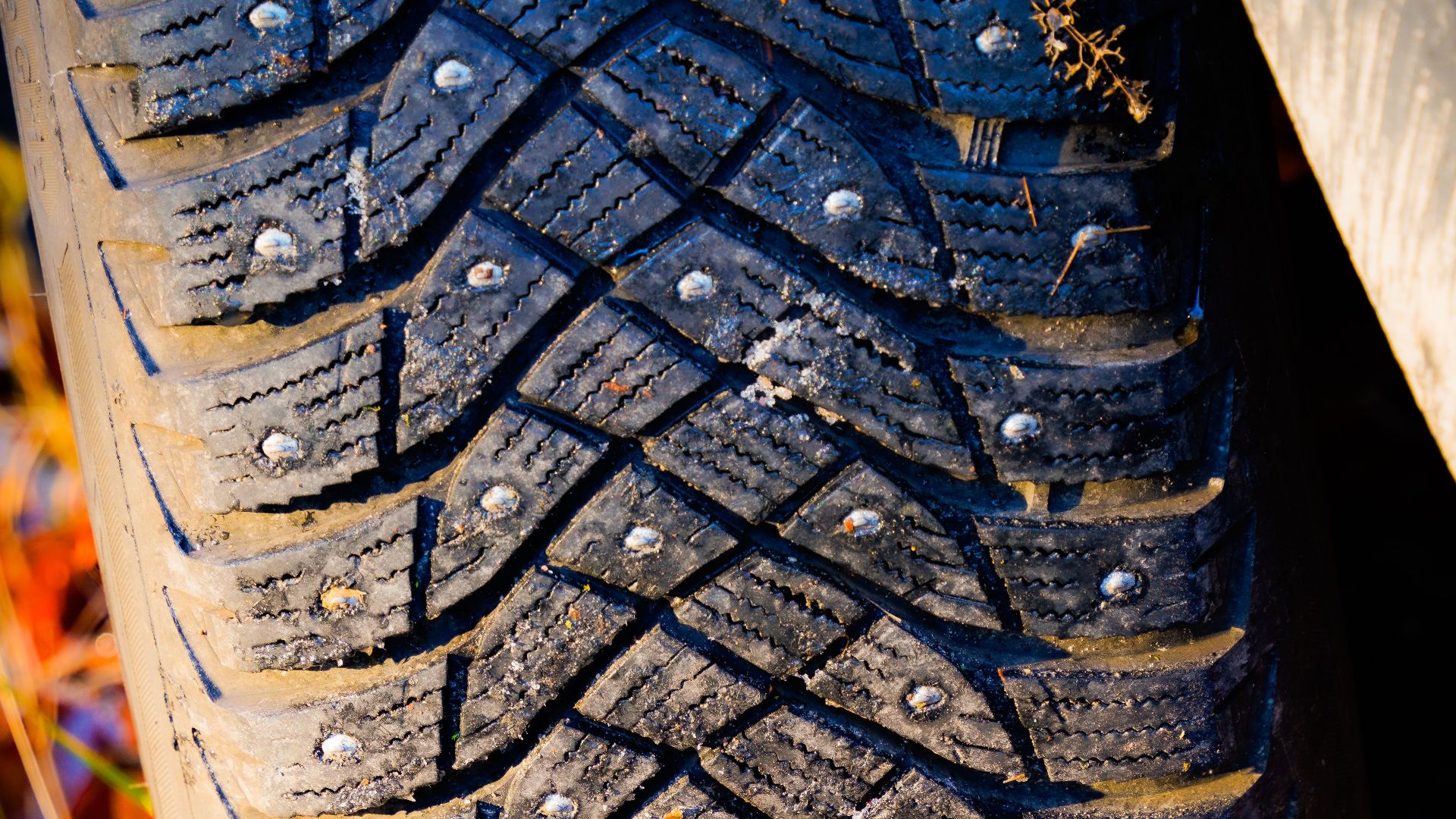 Close-up of a car tire on frosty autumn leaves, showcasing winter readiness.