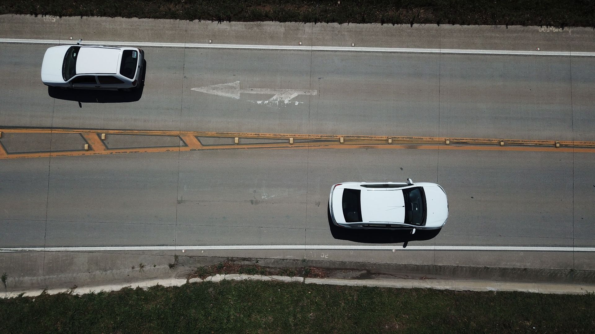Aerial shot of two white cars on a highway with directional markings.