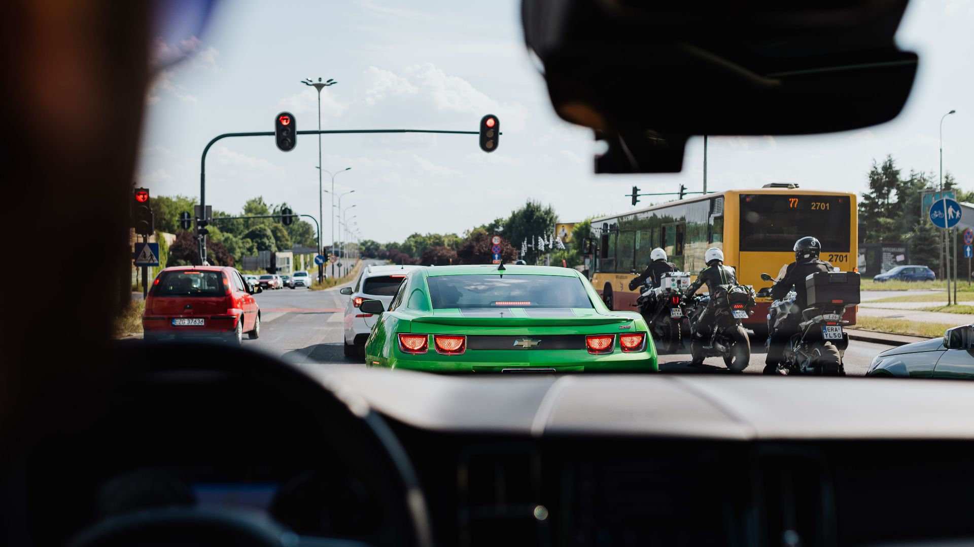 Street view of traffic with vehicles, bus, and motorcycles from a car's interior on a sunny day.