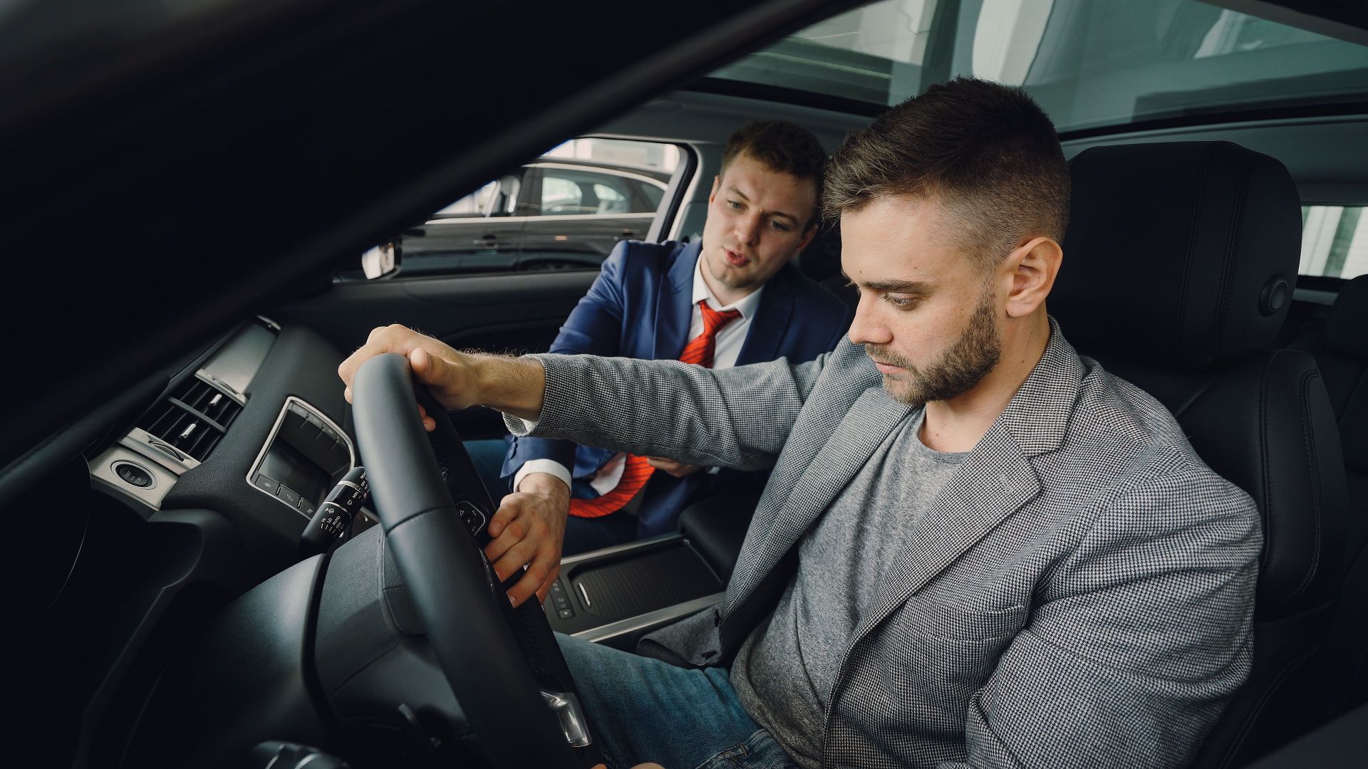Salesman demonstrating car features to potential buyer inside vehicle showroom.