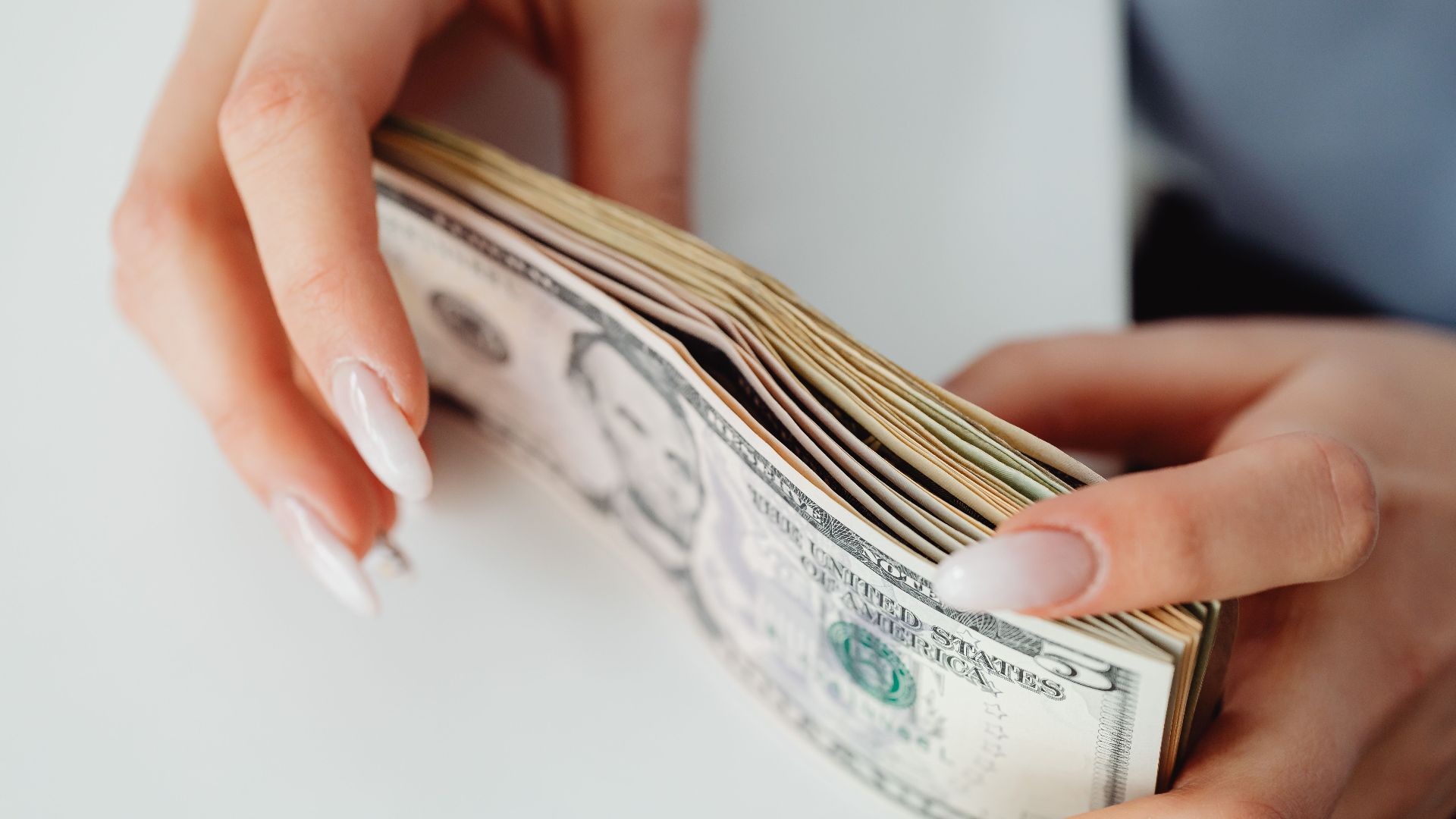 Hands carefully holding a stack of US dollar bills, representing finance and currency.