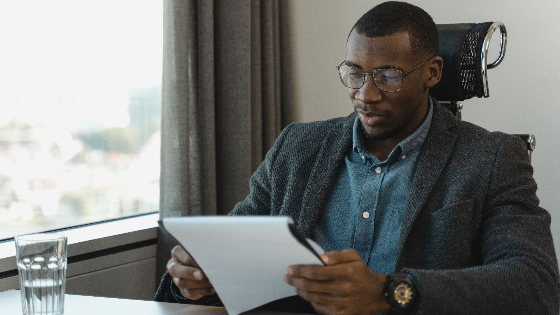 A focused businessman in eyeglasses reviewing documents at his office desk, providing a professional workspace vibe.