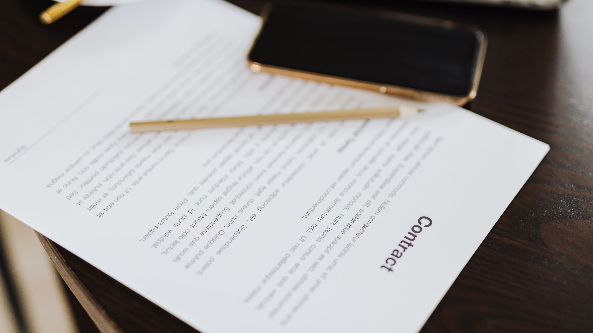 Close-up of a contract with office essentials like a laptop and coffee on a desk.