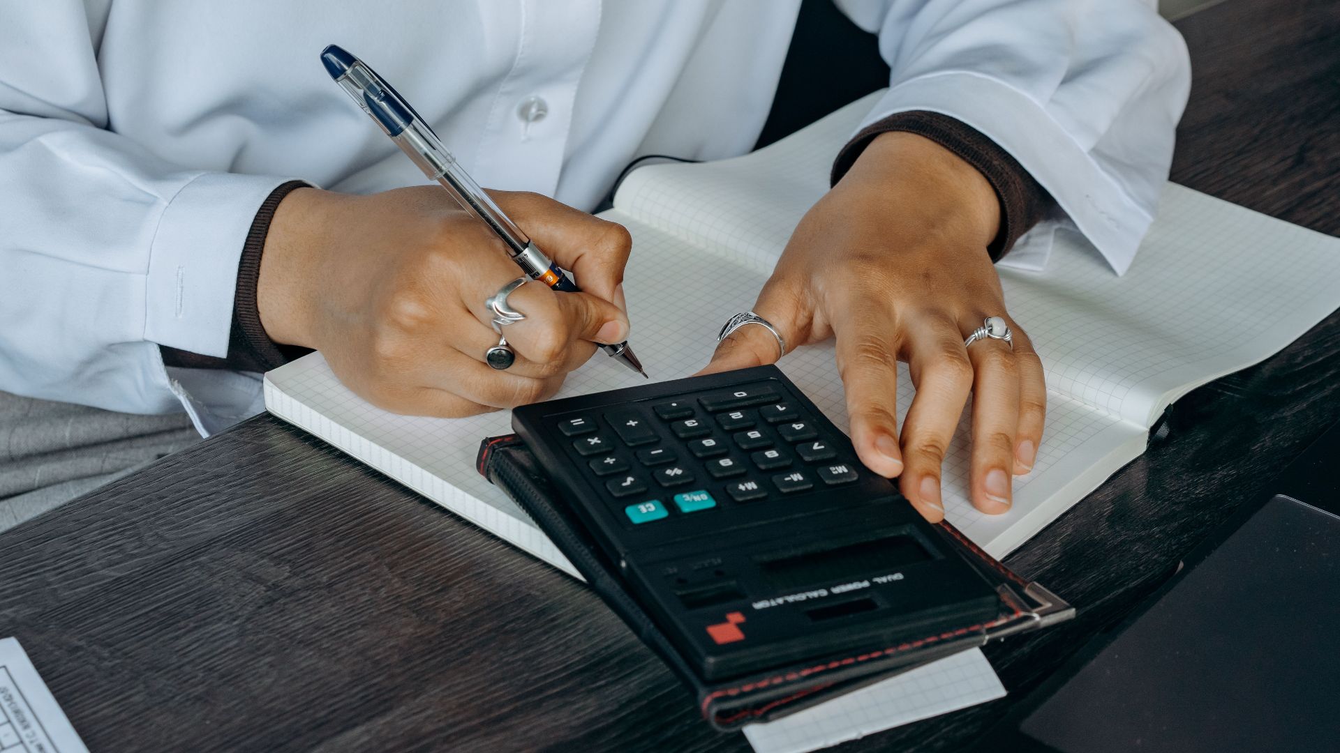 Close-up of a professional writing notes with calculator at a wooden desk.