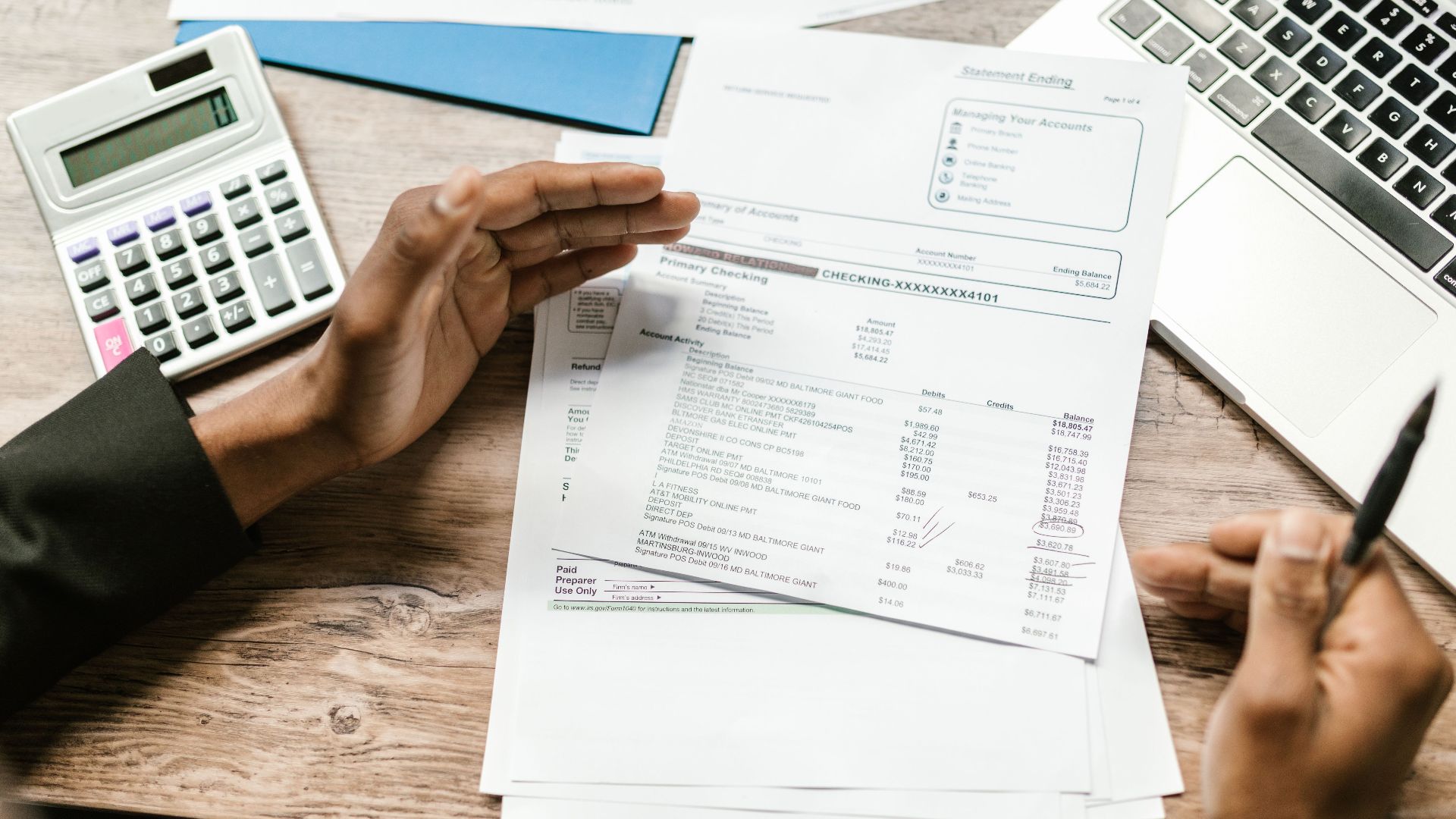 Hands holding financial documents with calculator and laptop on office desk, business analysis scene.