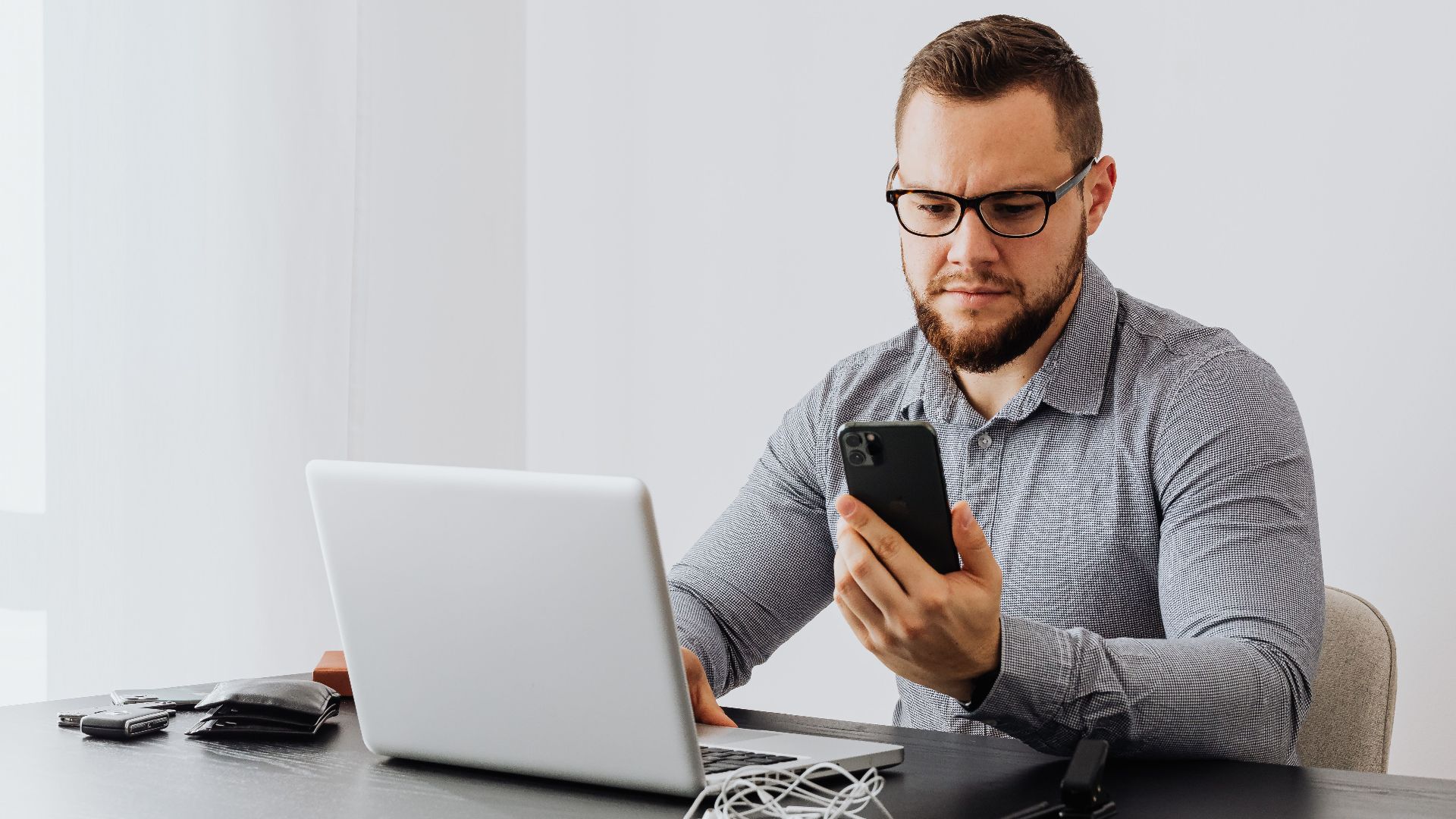 Professional man working at desk with laptop and smartphone, indoors.