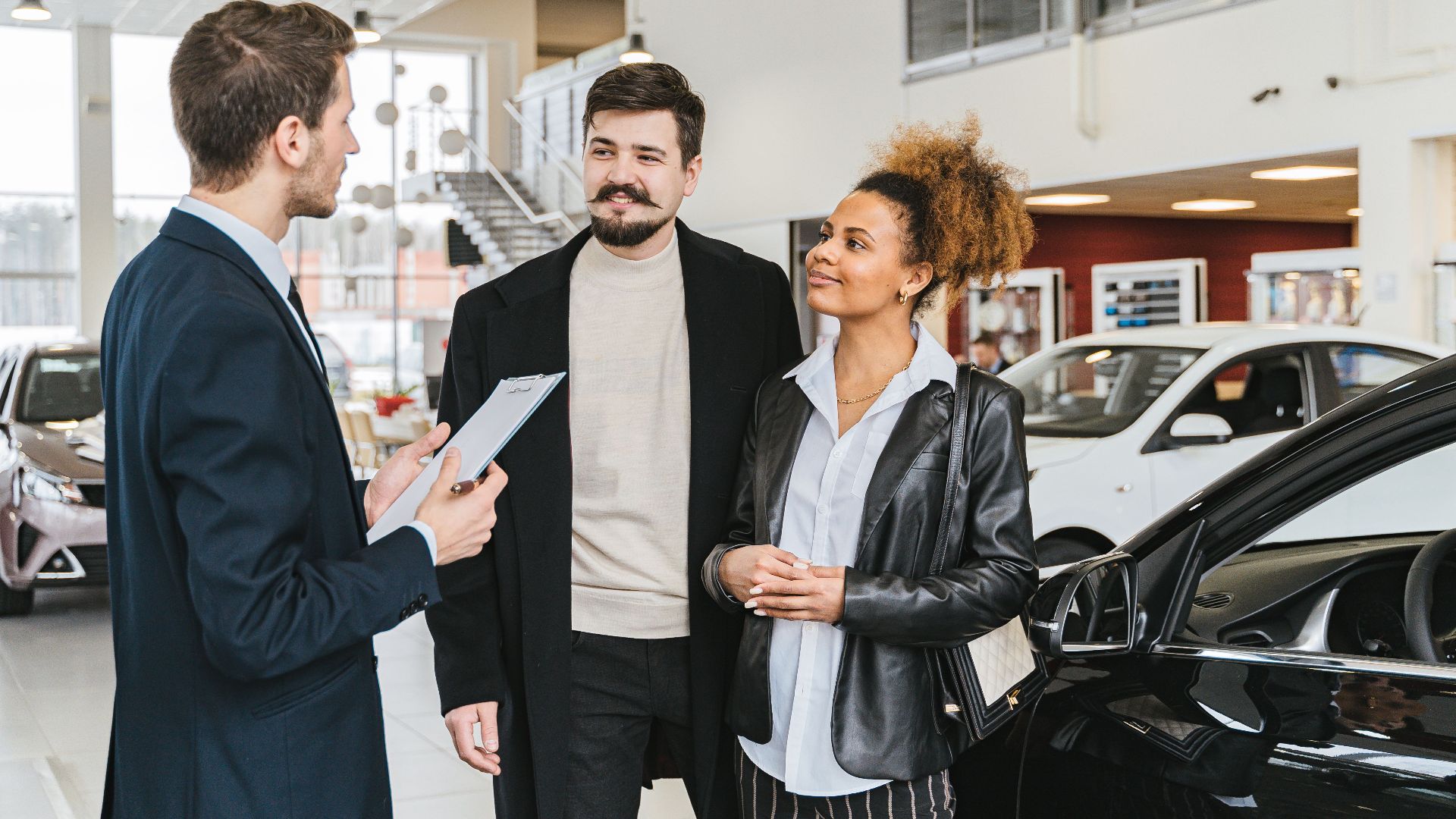 Couple discussing car purchase with salesman at indoor dealership, engaging conversation.