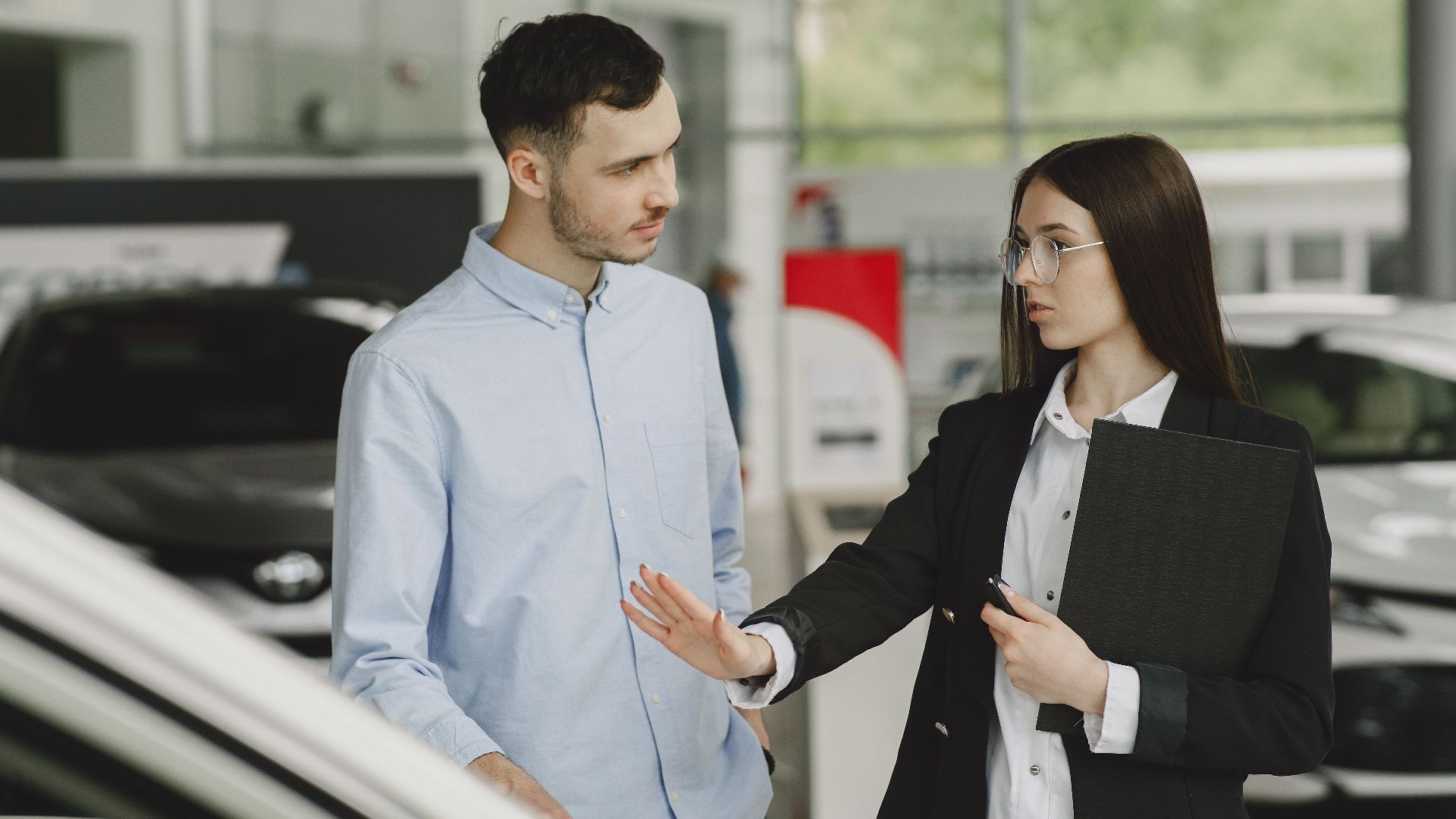 A salesperson and customer discussing car features in a dealership setting.