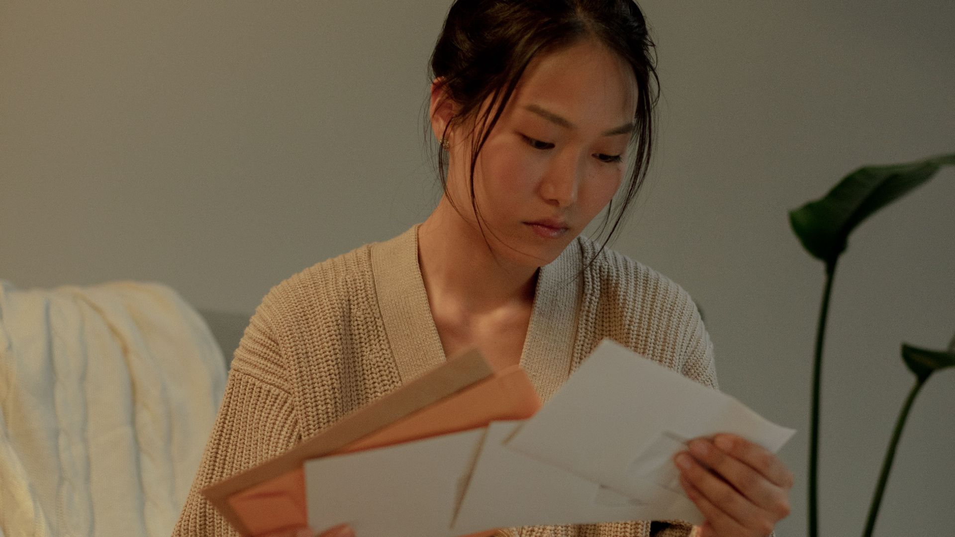 A woman seated in an armchair reads letters with focus, creating a warm, introspective mood.