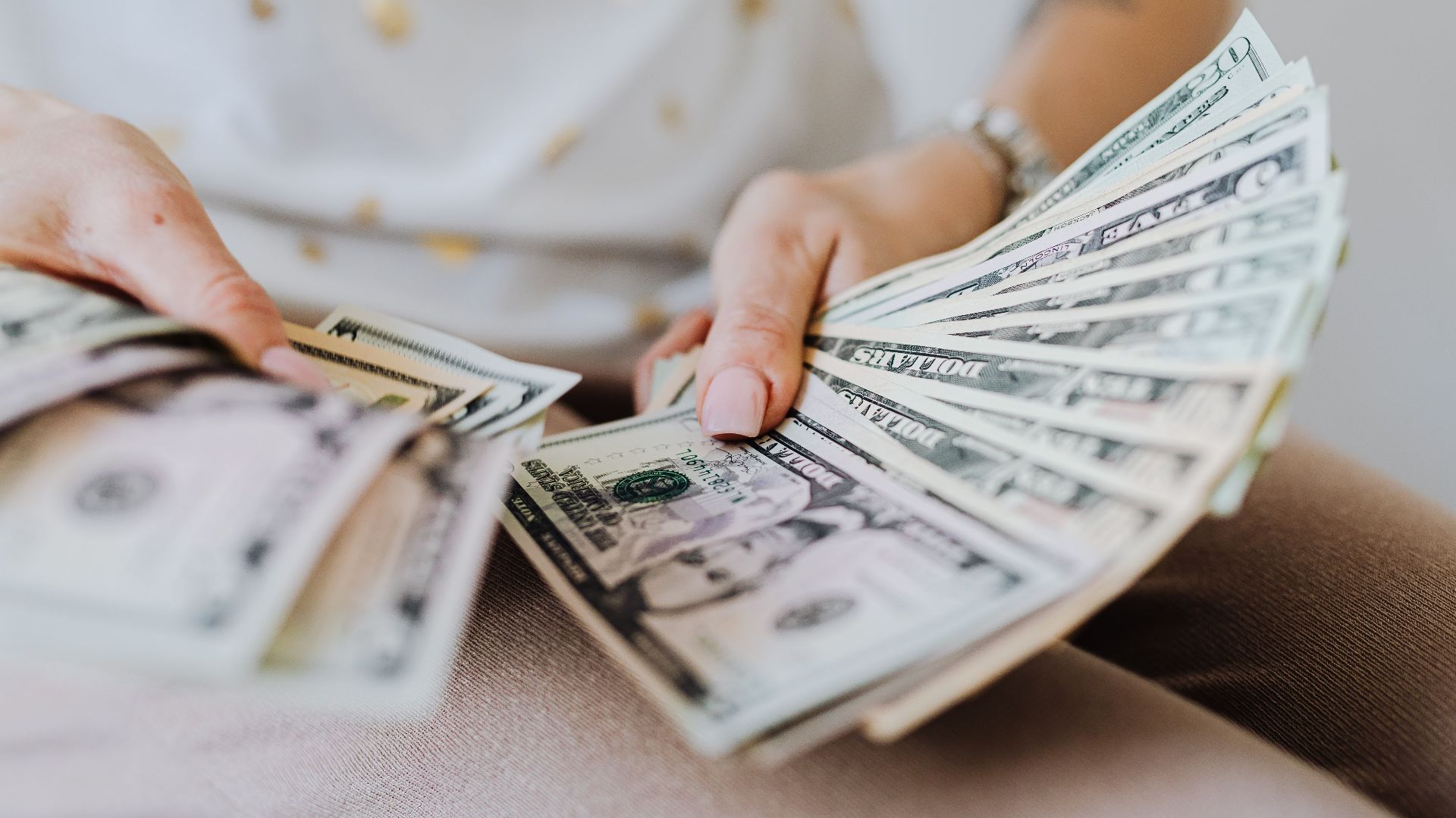 Close-up of hands holding and counting US dollar bills indoors.