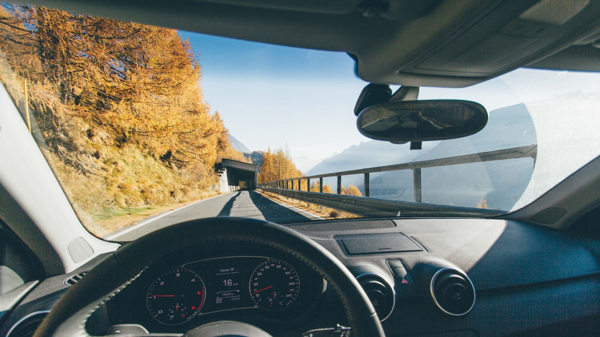 View from car interior driving through a scenic mountain road with autumn foliage and clear skies.