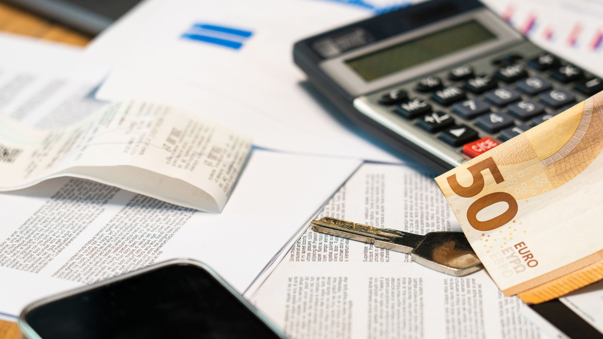 Flat lay of financial documents, euro note, calculator, smartphone, and key for budget management.