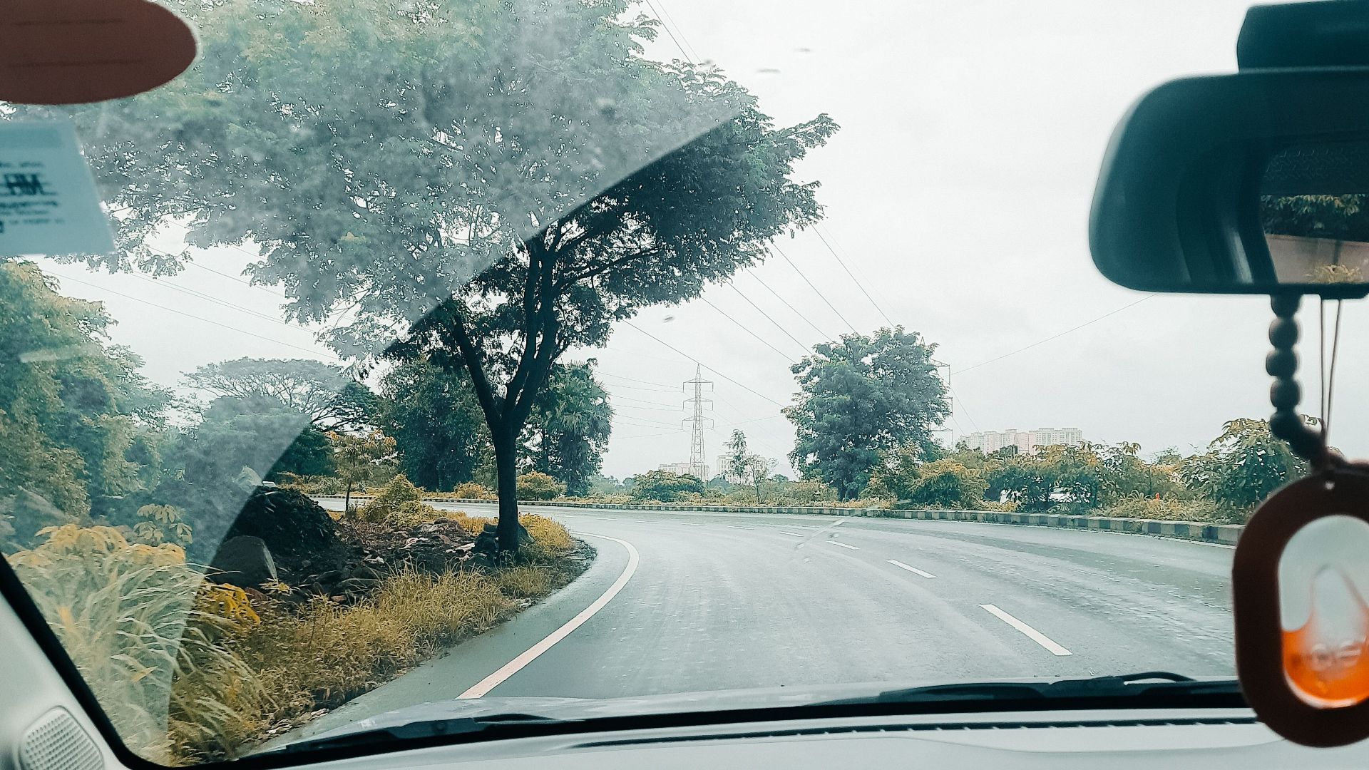 View from inside a car driving on a winding countryside road. Lush greenery and cloudy skies outside.