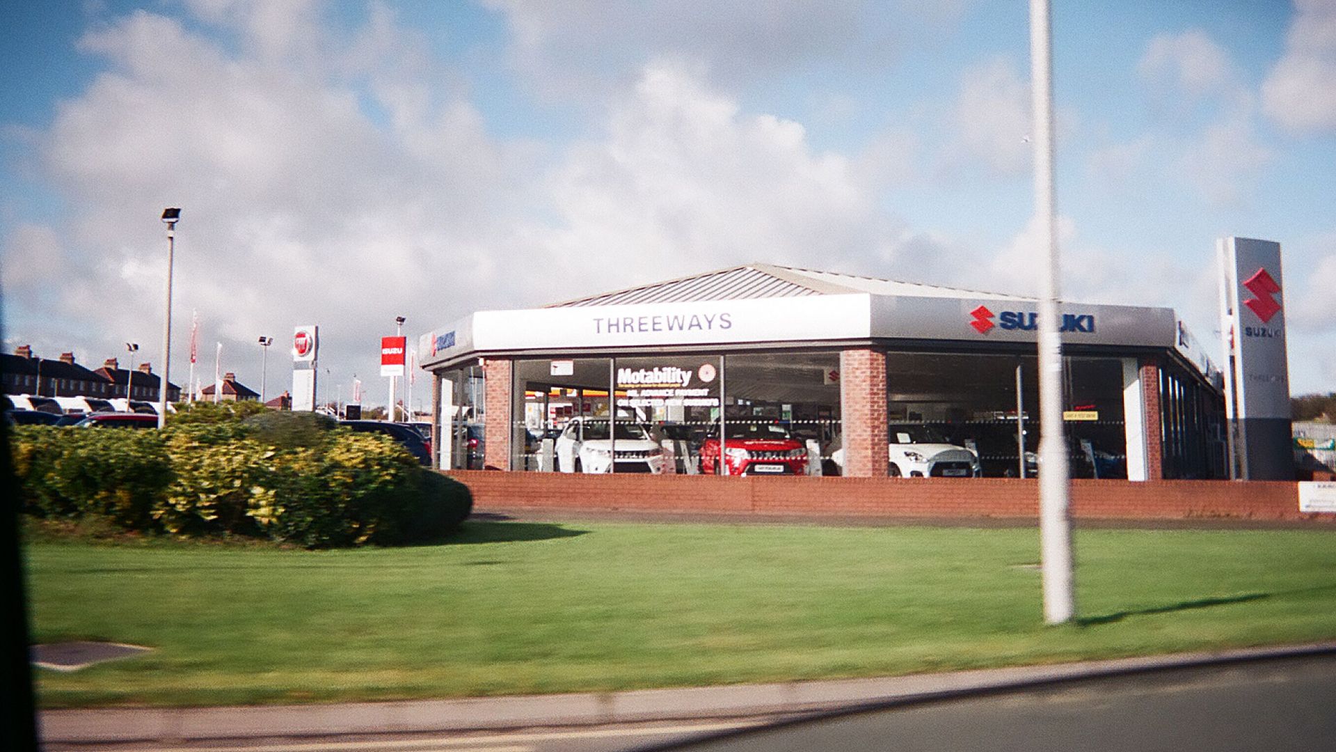 Exterior view of a car dealership featuring Suzuki automobiles under a bright sky.