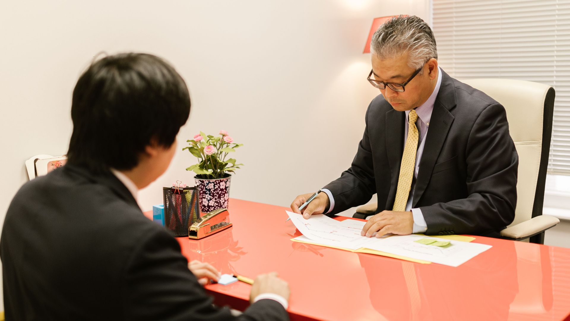 Two professionals discussing documents in a modern office with a red desk.