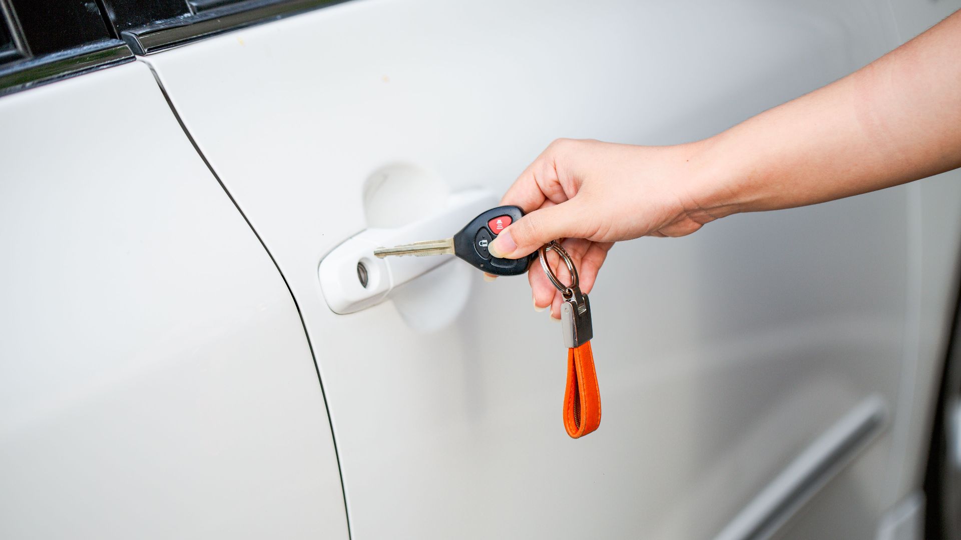 Close-up of a hand unlocking a white car door with a metal key and key fob.