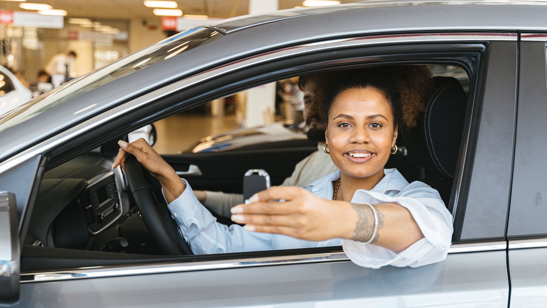 Smiling woman sitting in her new car holding keys, celebrating purchase.