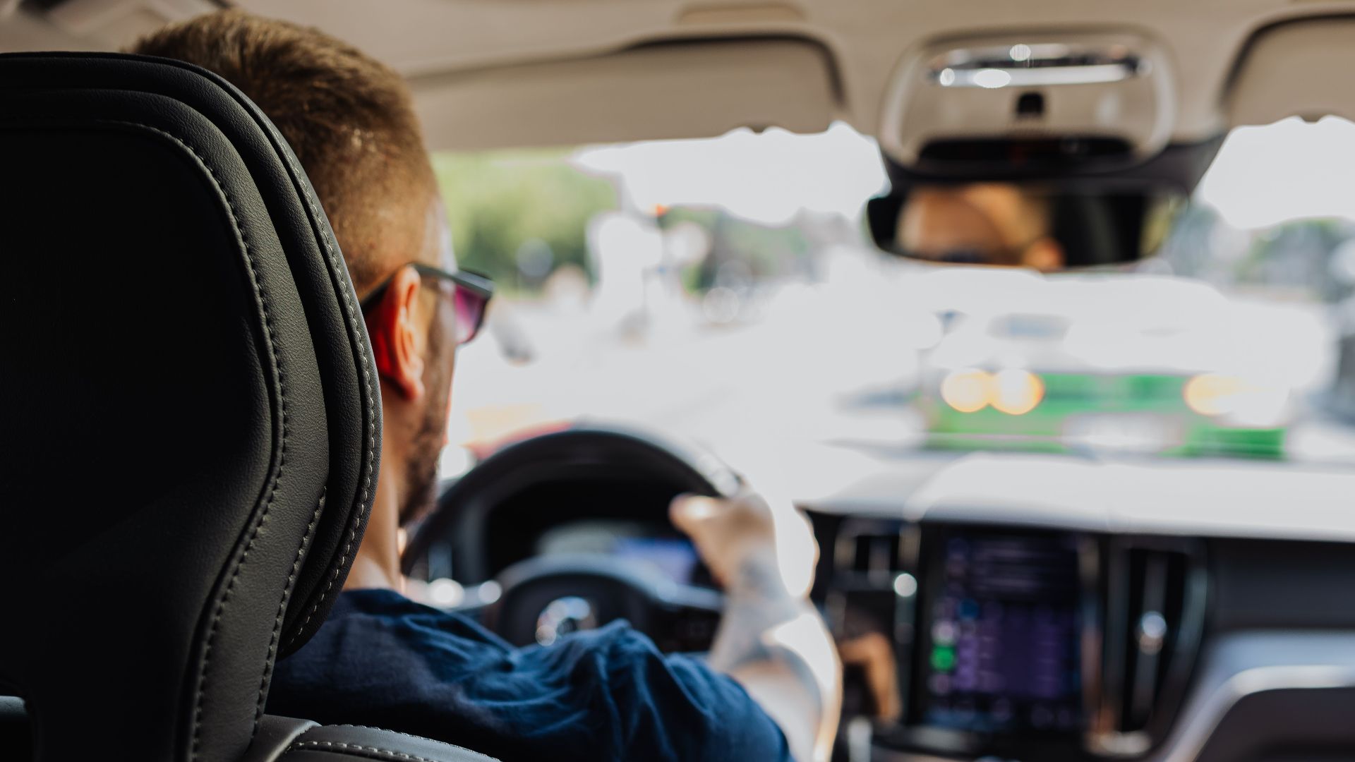 Close-up of a man driving a modern vehicle from behind with a blurred urban background.