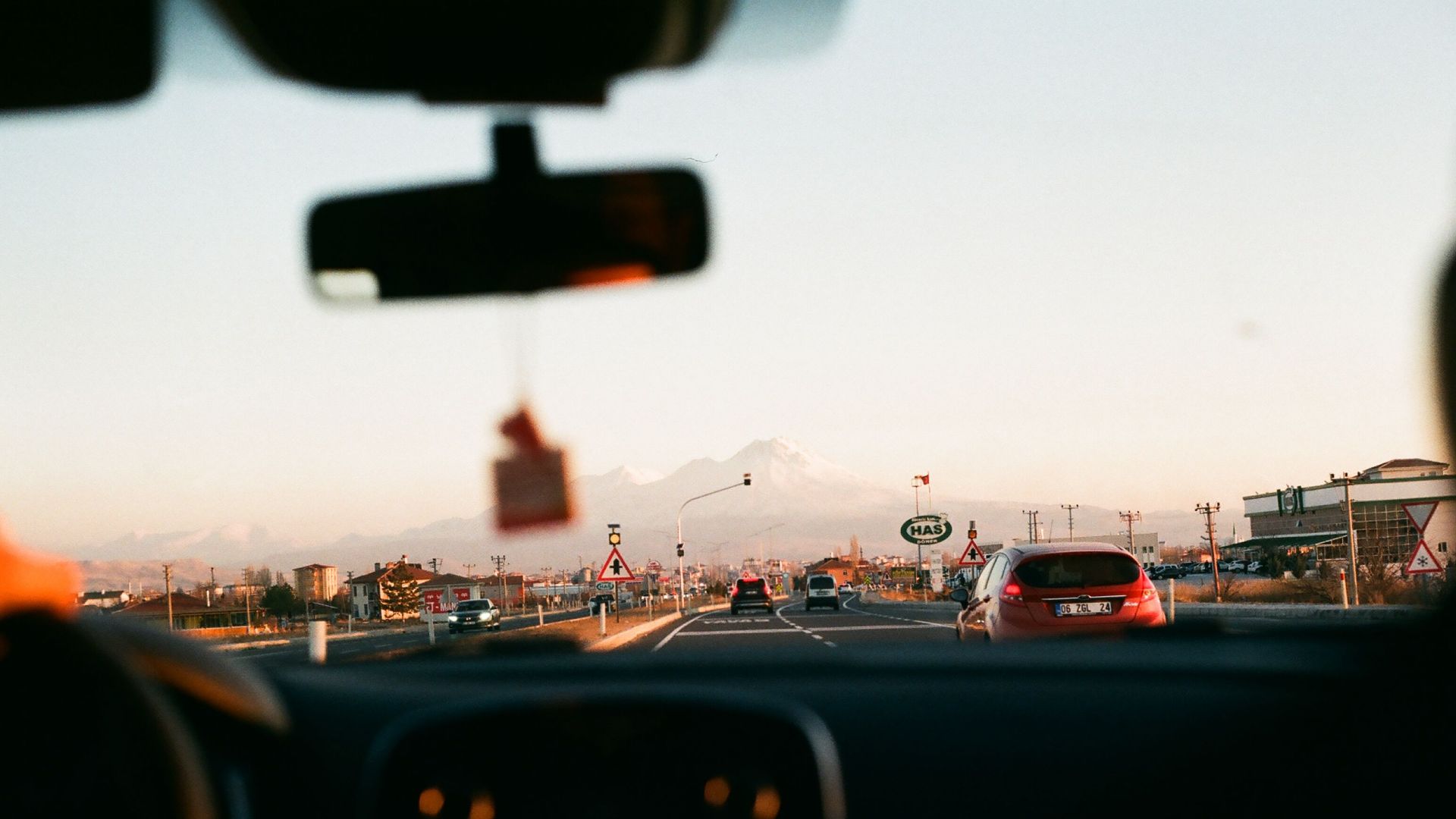 View from inside a car driving towards a mountainous landscape during sunset with beautiful sky.