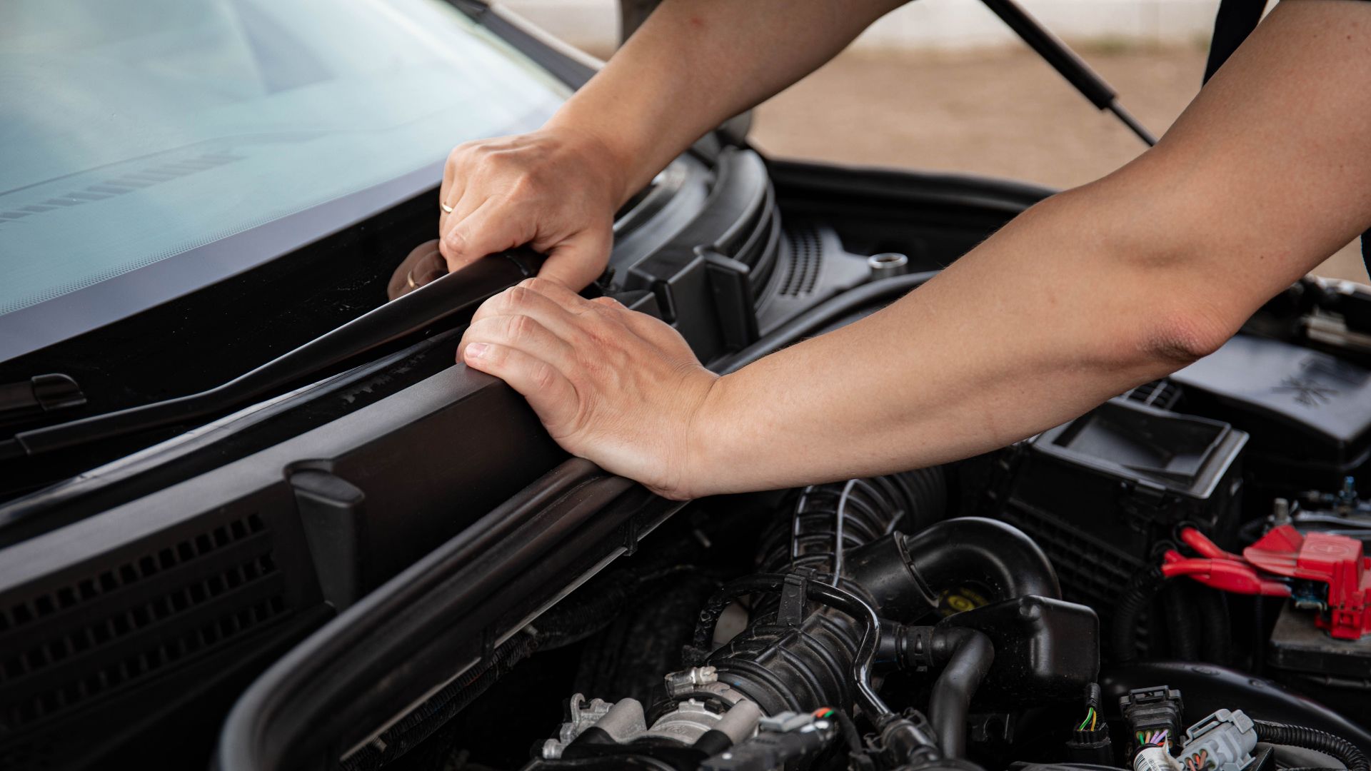 Close-up of hands repairing a car engine outdoors, focusing on automotive maintenance.
